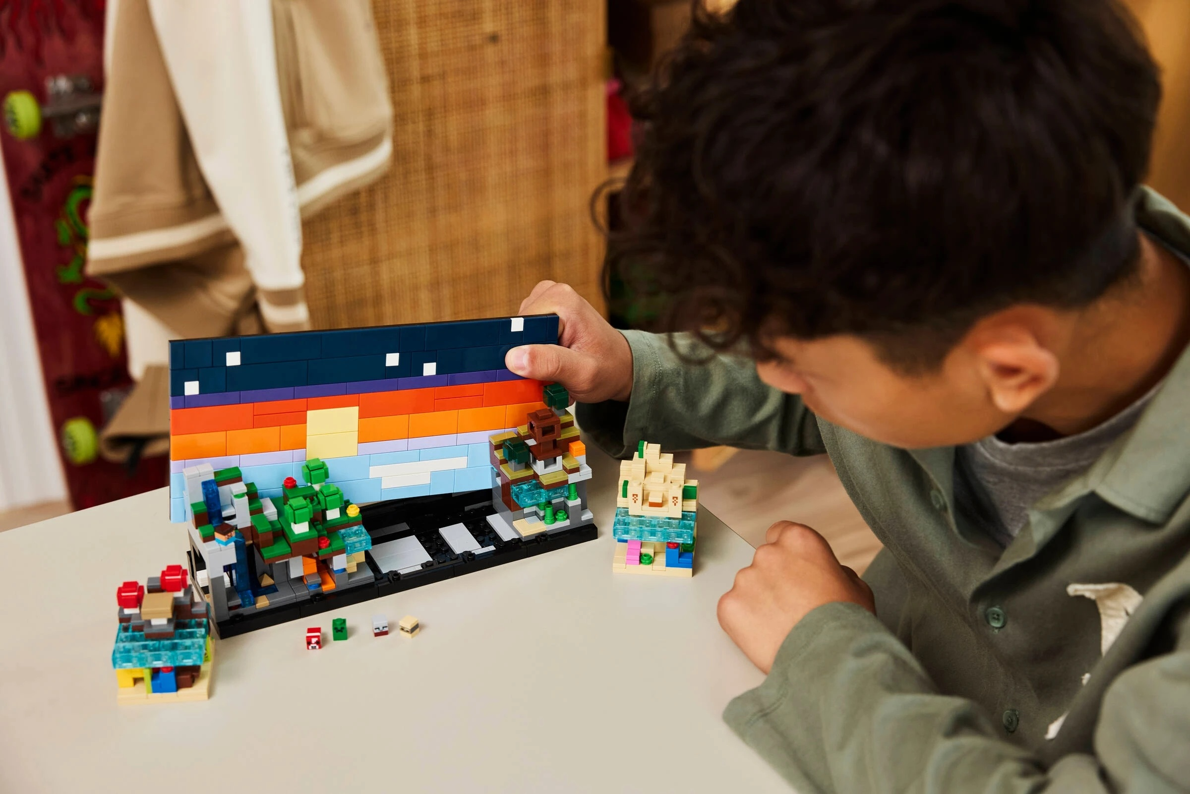 Chłopiec buduje kolorowy model Lego z drzewami i niebem w gradientach.