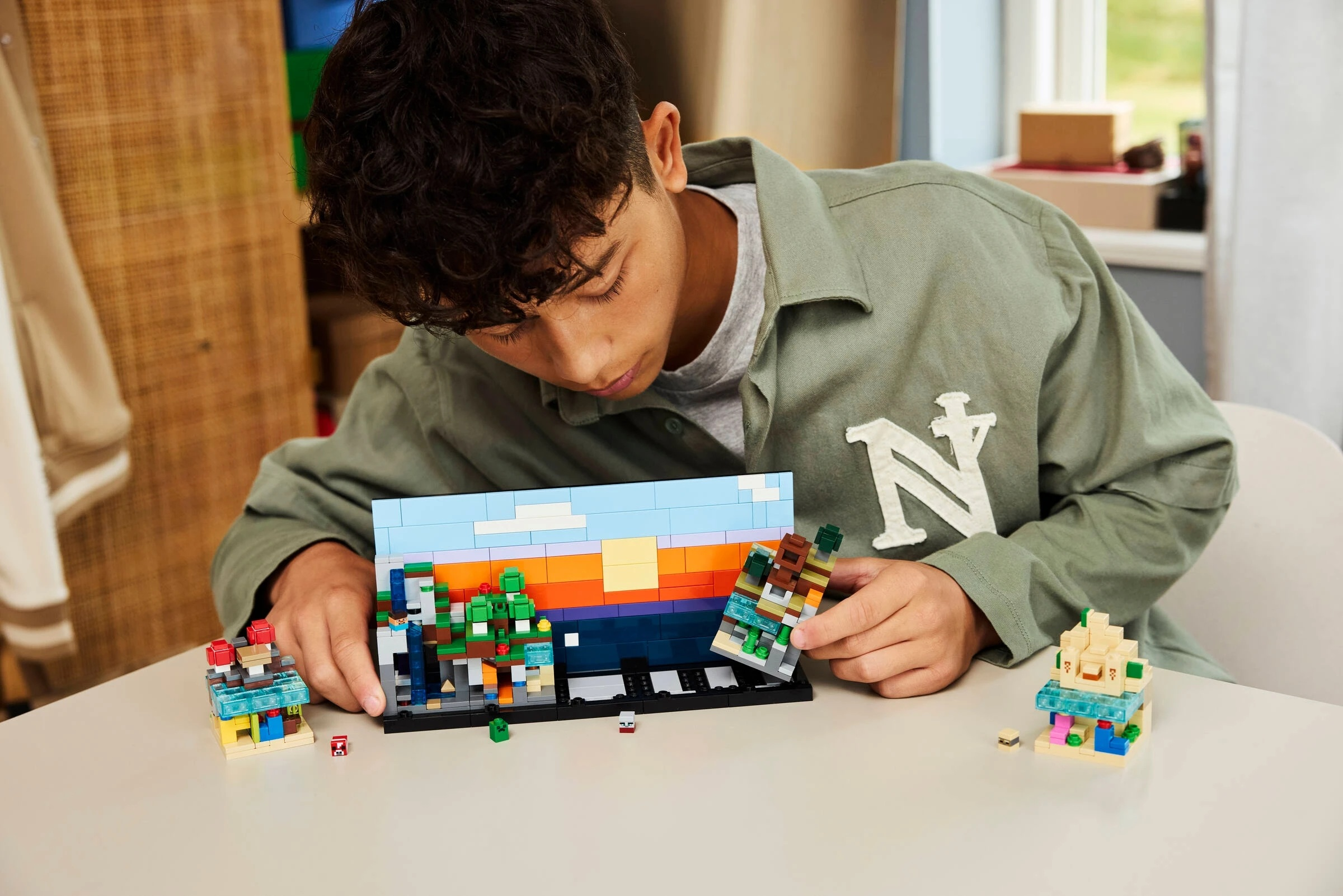 Chłopiec buduje scenę z Minecrafta z kolorowych klocków Lego, z domkami i drzewami.
