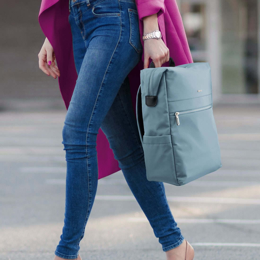 Eine Frau in Jeans und pinkem Mantel trägt einen blauen Rucksack.