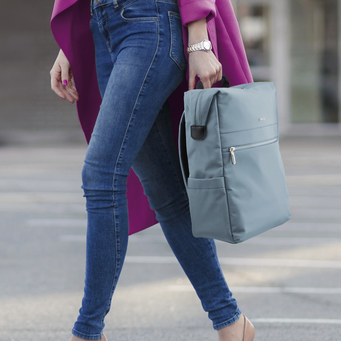 Eine Frau in Jeans und einem pinken Mantel trägt einen hellblauen Rucksack.
