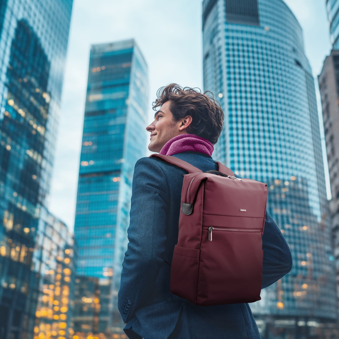 Mann mit Rucksack und Schal vor Wolkenkratzern.