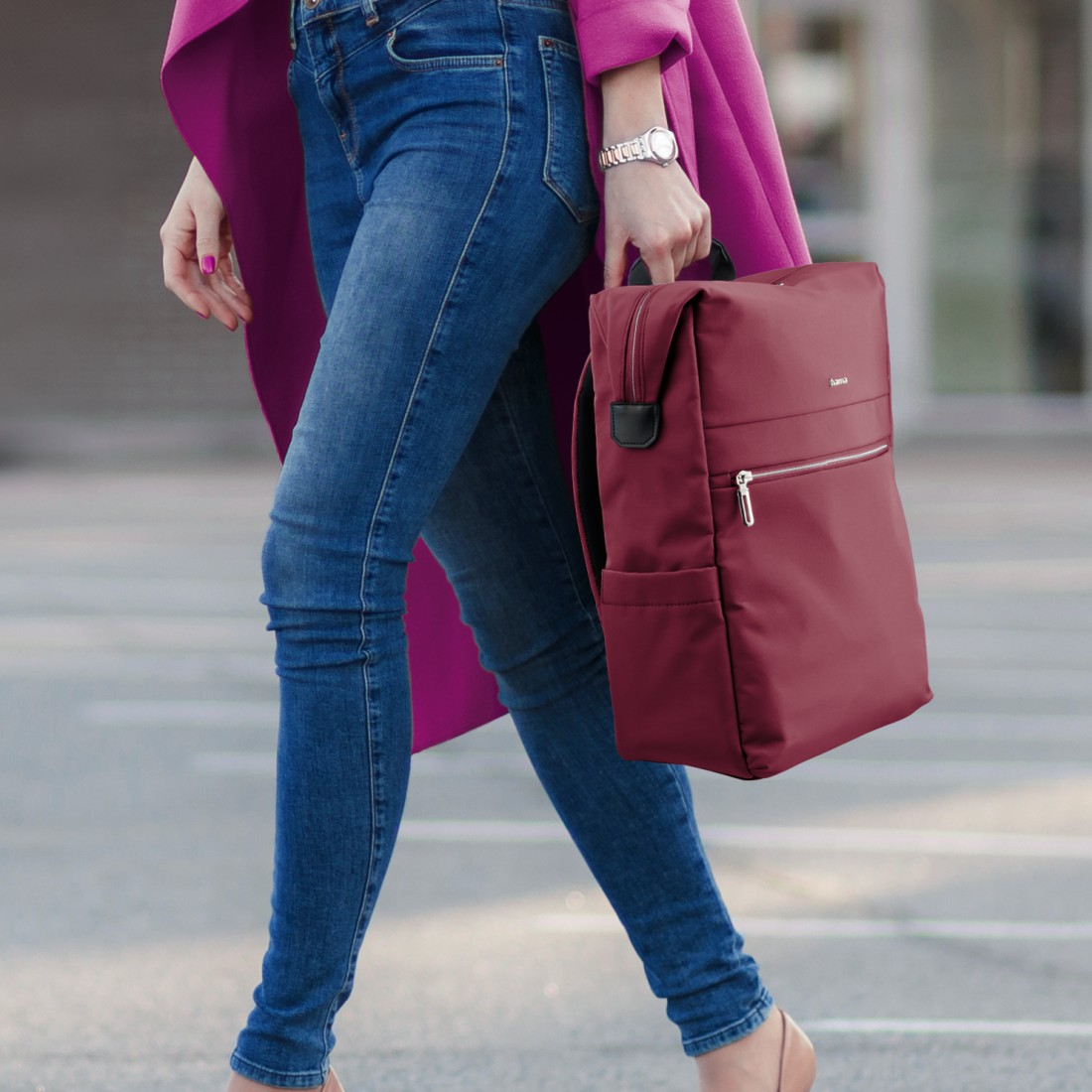Eine Frau in Jeans und pinkem Mantel trägt einen weinroten Rucksack.