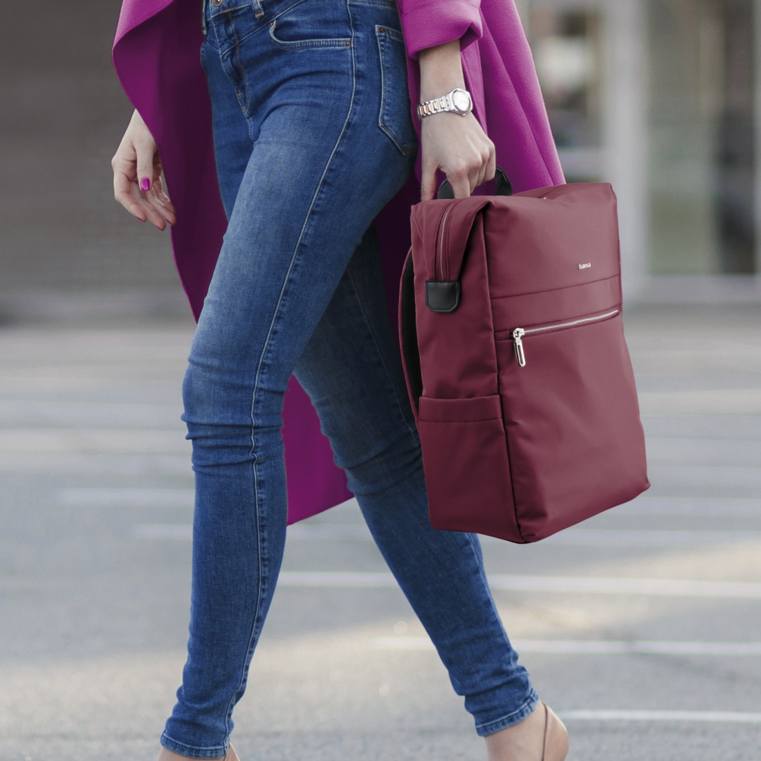 Eine Person mit Jeans und pinkem Mantel trägt einen burgunderroten Rucksack.