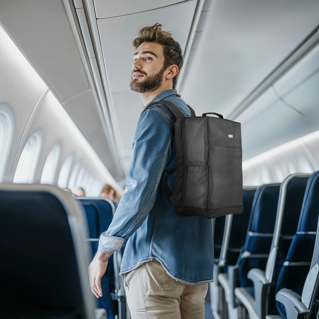 Mann mit Rucksack im Flugzeuggang, blickt nach rechts.