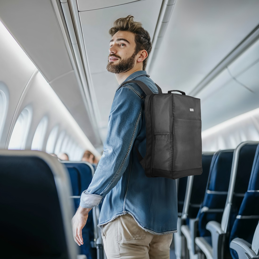 Mann mit schwarzem Rucksack geht den Flugzeuggang entlang, trägt Jeanshemd und Khakihose.