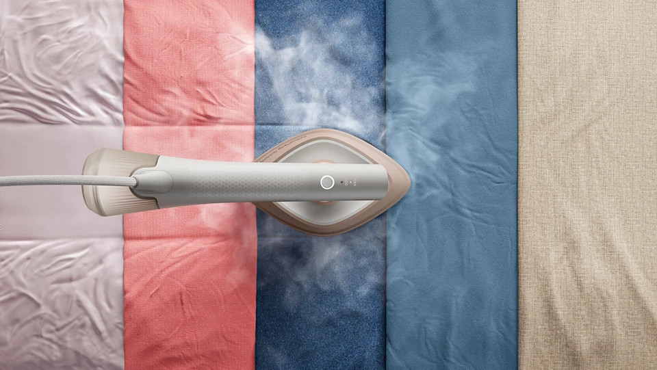 Parownica prasuje tkaniny w kolorach różowym, koralowym, niebieskim i beżowym.