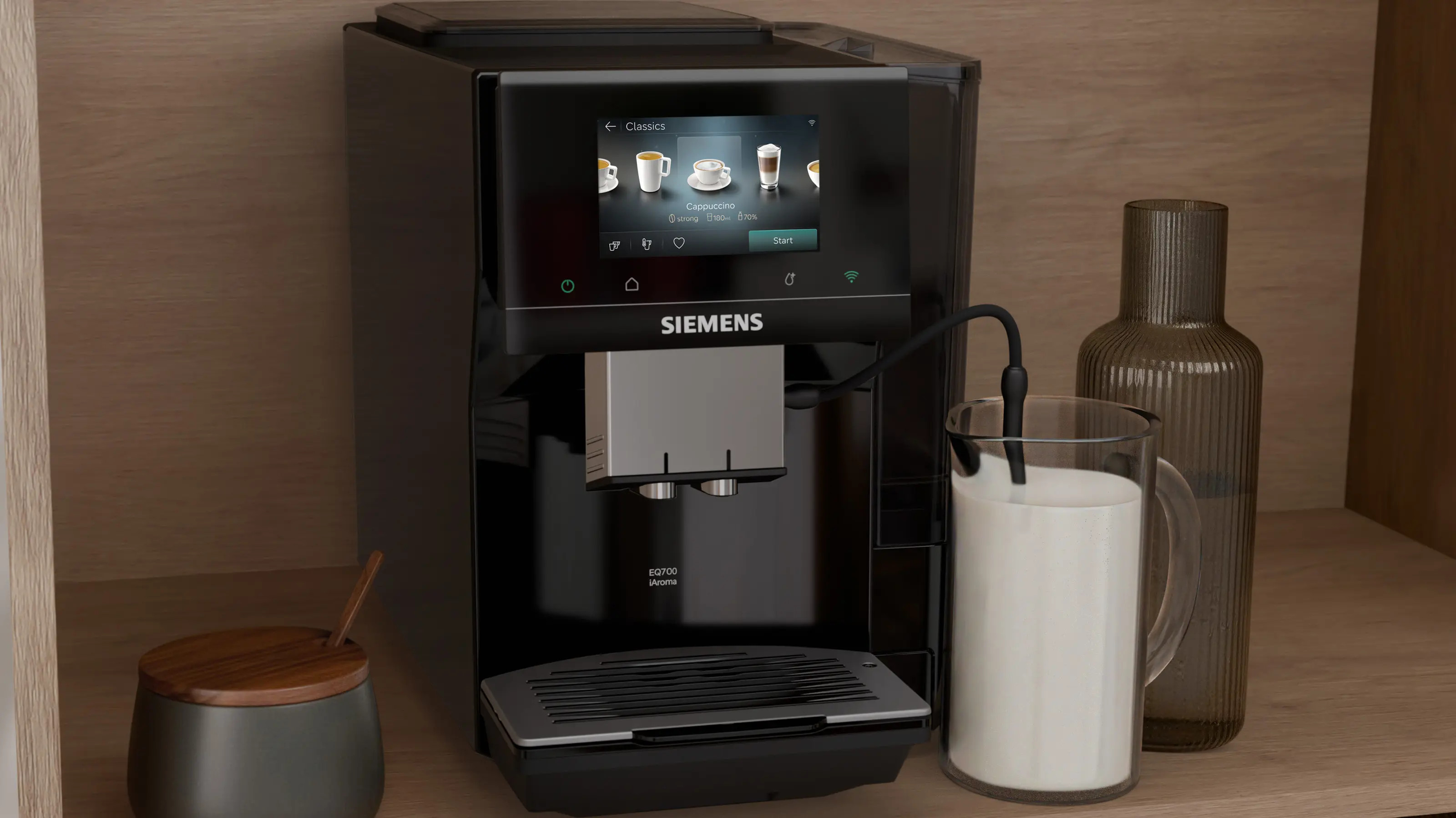 Czarny ekspres do kawy z ekranem dotykowym, obok szklanka mleka i karafka.