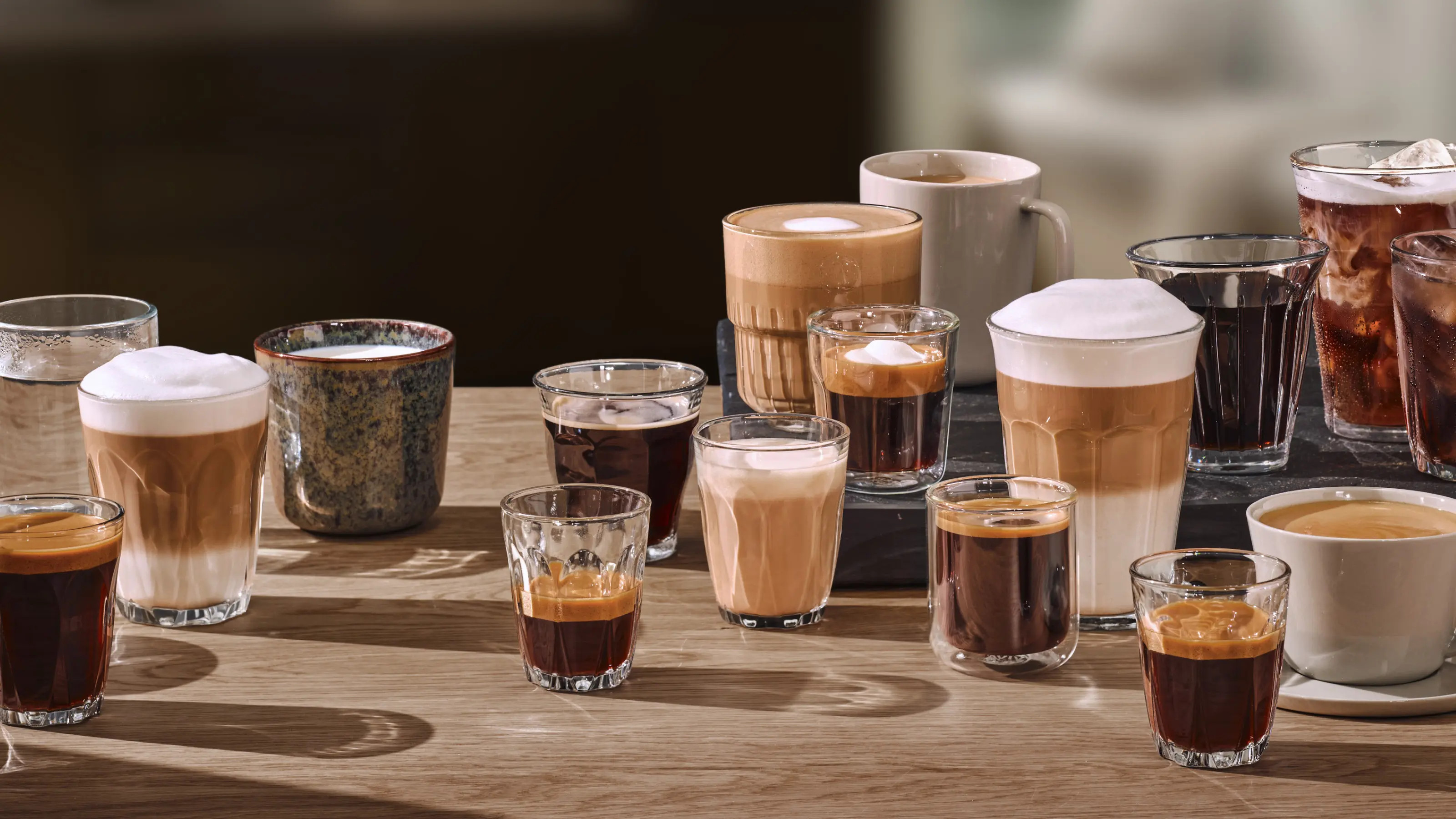 Asortyment napojów kawowych w szklankach i kubkach na drewnianym stole.