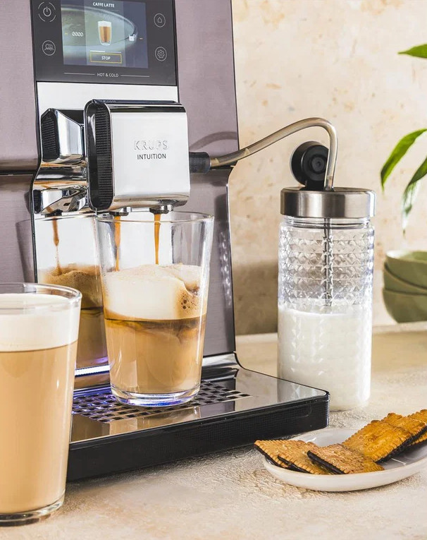 Ekspres do kawy parzy latte do szklanki, obok pojemnik na mleko.