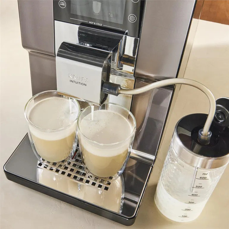 Ekspres do kawy z dwoma pełnymi szklankami i pojemnikiem na mleko.