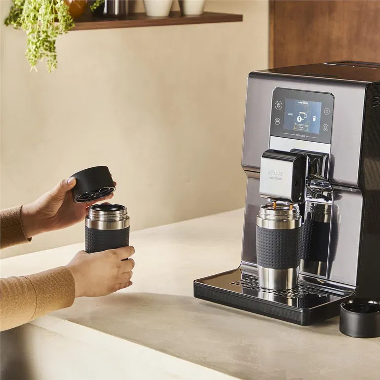 Osoba zakłada pokrywkę na kubek z kawą pod ekspresem.