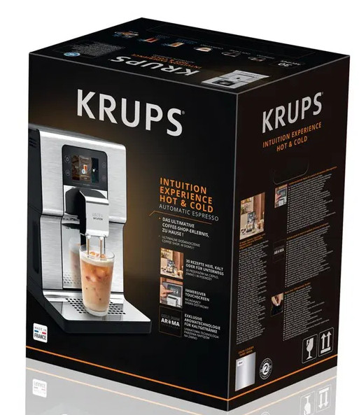 Automatyczny ekspres do kawy Krups ze szklanką i napojem, na czarnym opakowaniu.