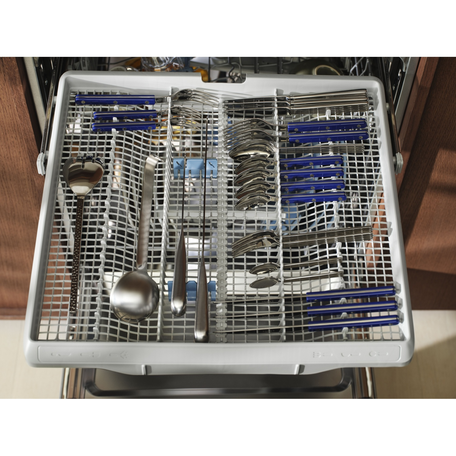 Cestello lavastoviglie con posate blu e metalliche. Organizzato per il lavaggio.
