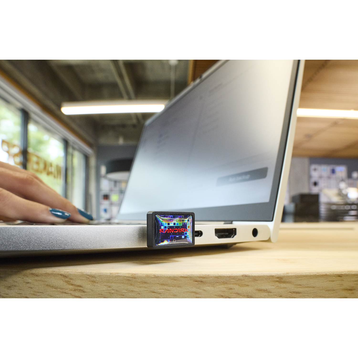 A SanDisk USB drive plugged into a laptop, with a hand typing in the background.