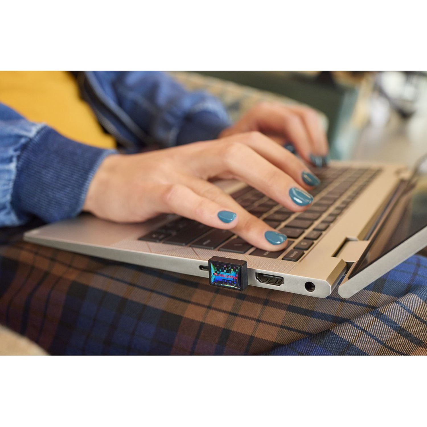 Close up of hands typing on a laptop, a USB device plugged in.