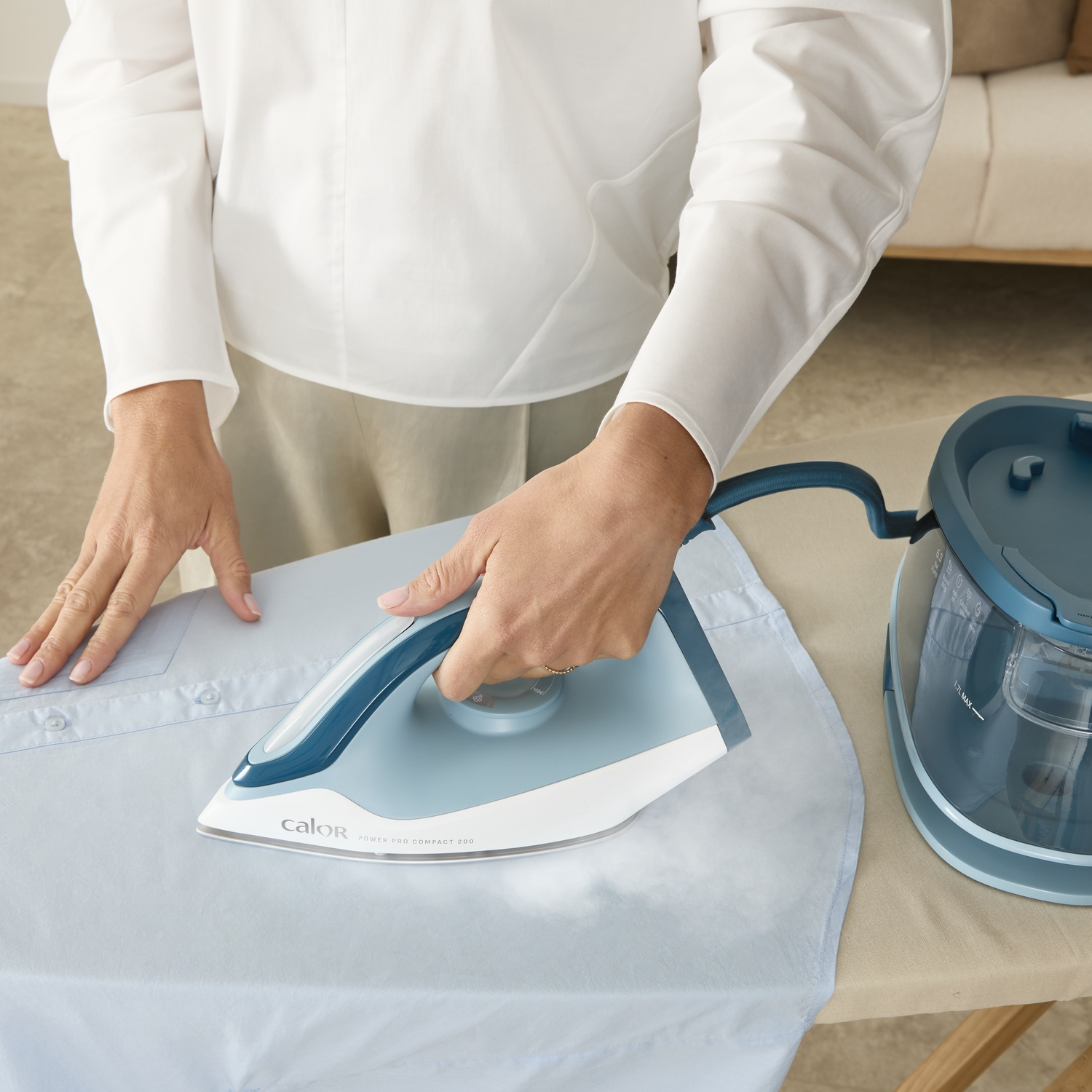 A person irons a blue shirt on an ironing board with a steam iron.