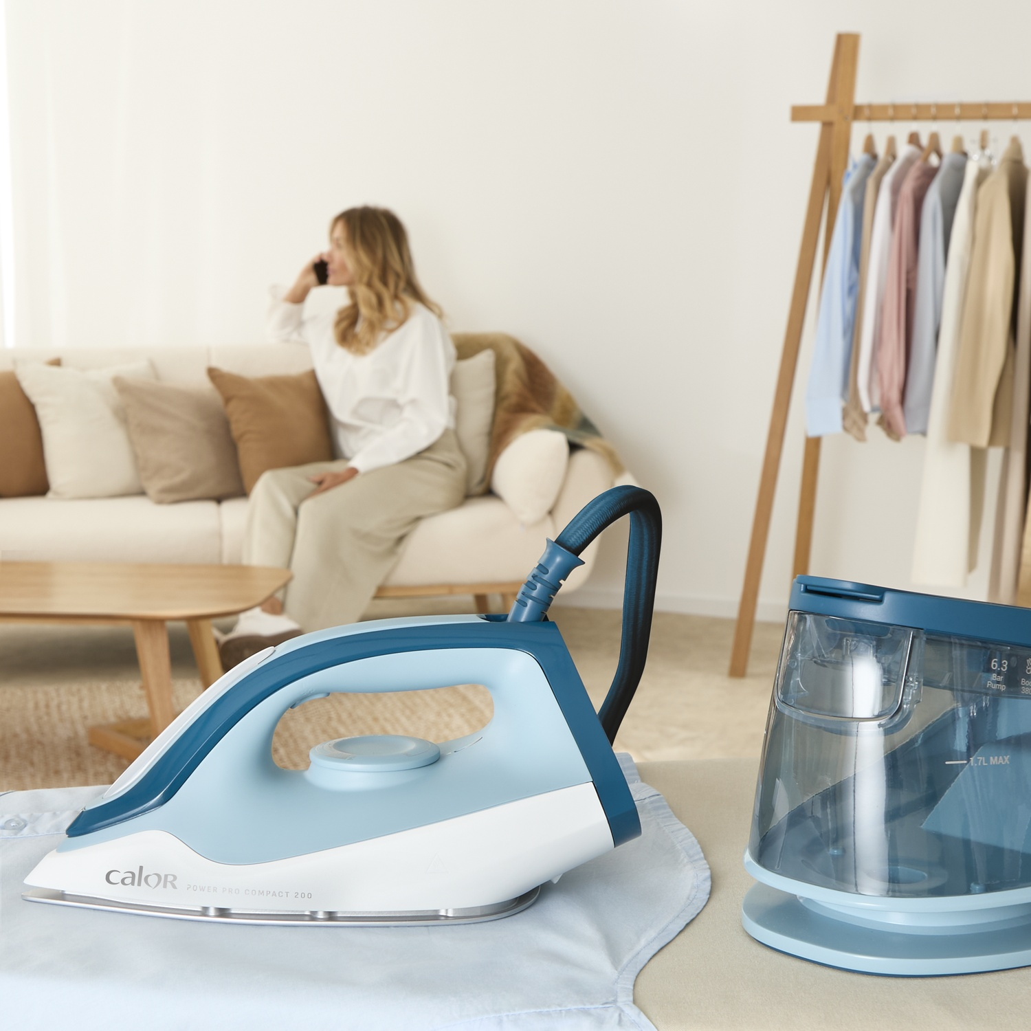 A woman talks on the phone on a sofa. An iron and a steam generator are on display.