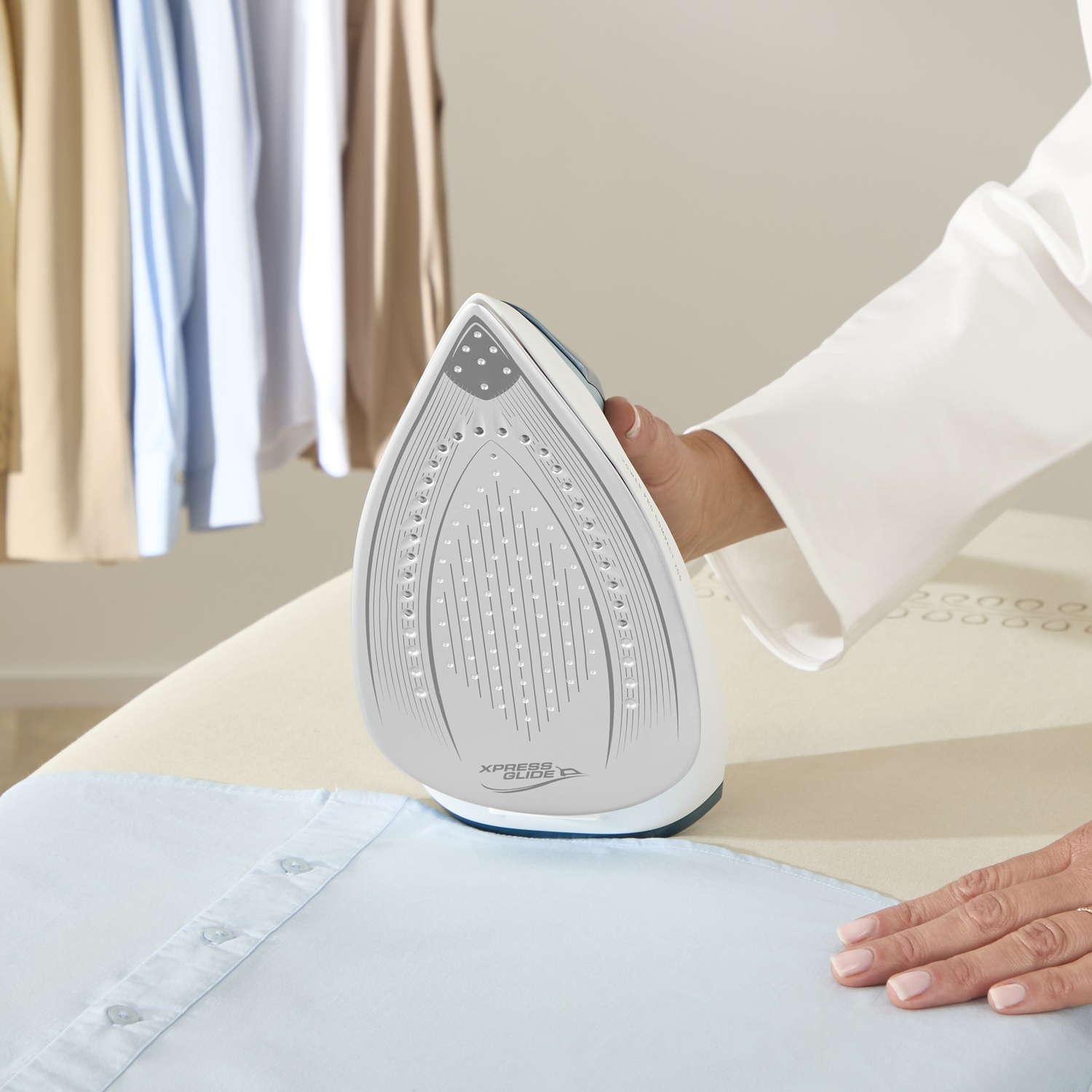 A hand holds an iron over a light blue shirt on an ironing board.