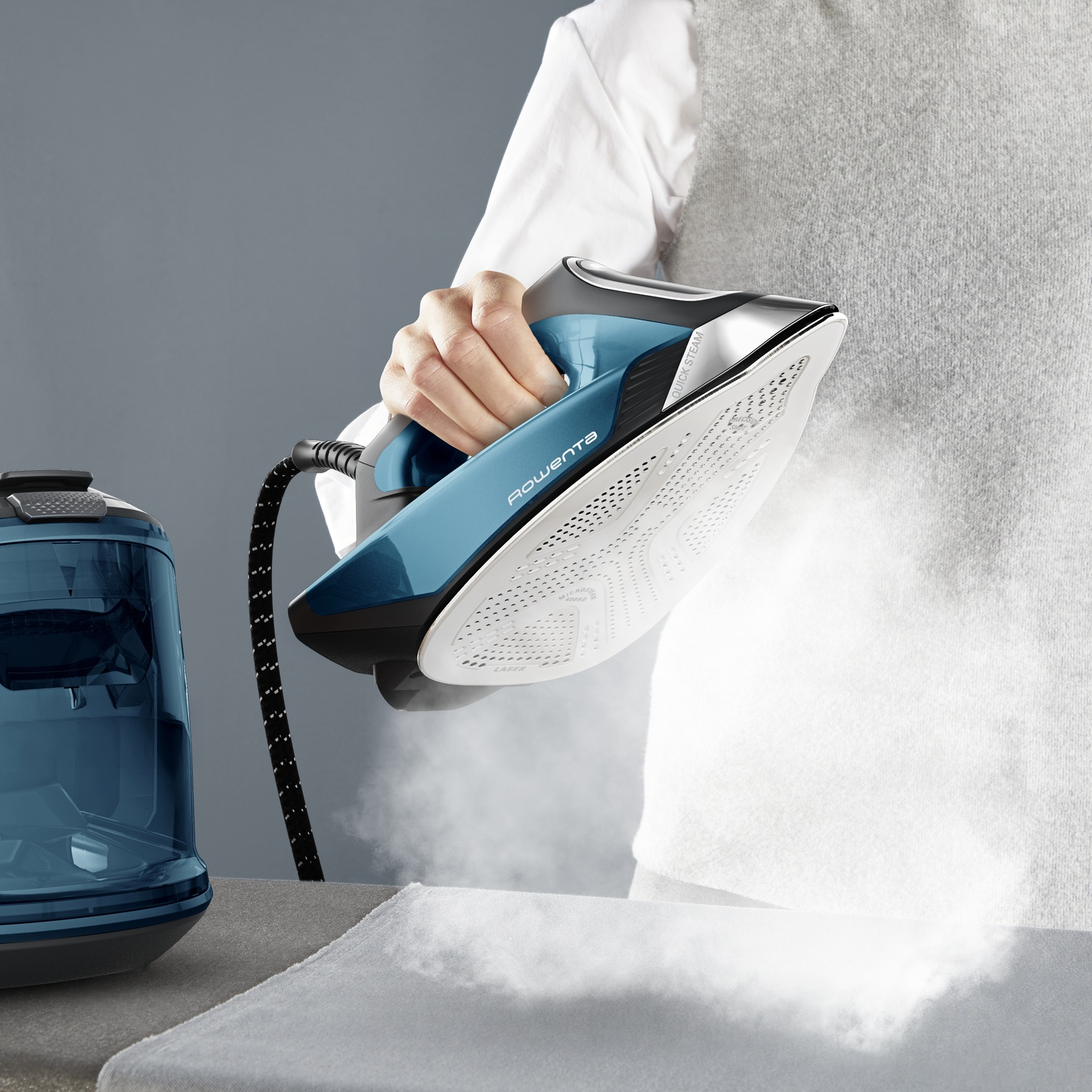 Une main tient un fer à vapeur bleu. De la vapeur s'échappe.