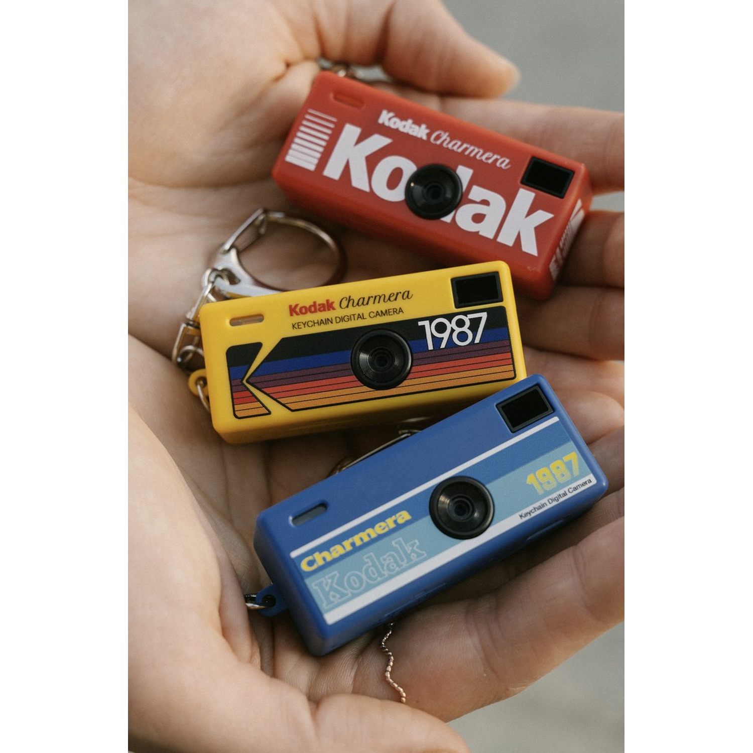 Drie Kodak Charmera sleutelhanger camera's in rood, geel en blauw rusten in handen.