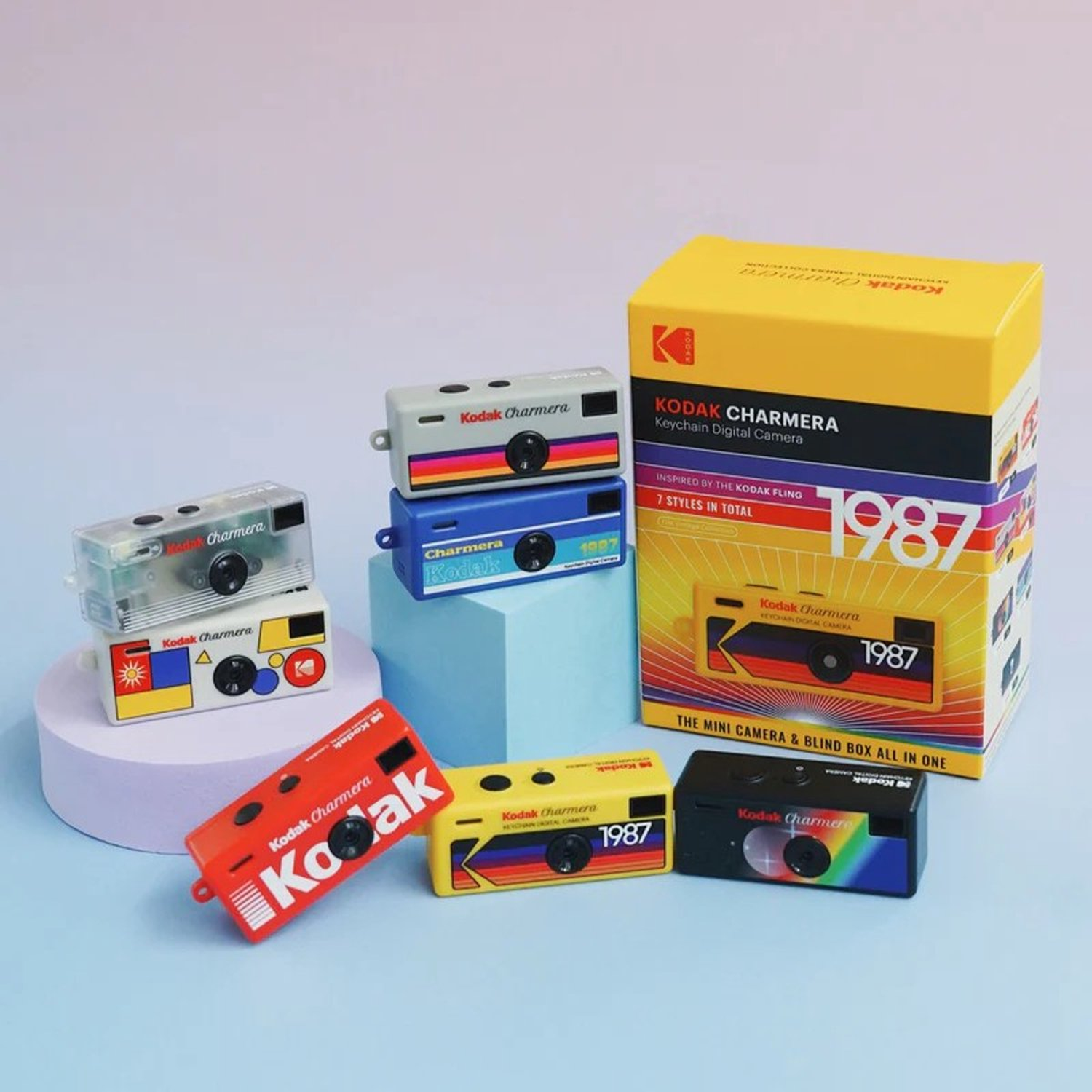 Verschillende kleurrijke Kodak Charmara minicamera's en een doos gerangschikt op een blauwe en paarse achtergrond.