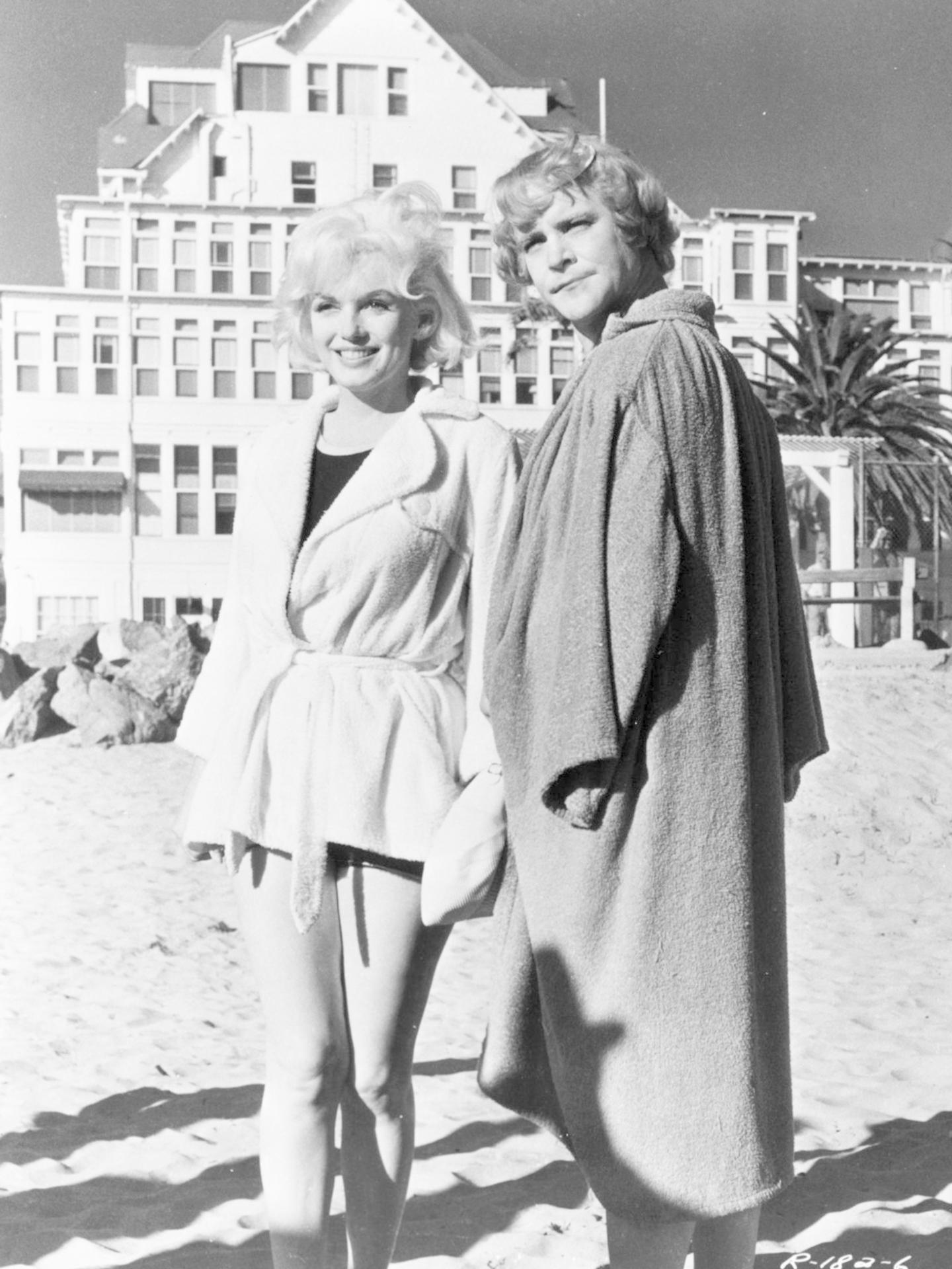 Zwei Frauen stehen am Strand vor einem Gebäude. Eine trägt einen weißen Bademantel, die andere einen grauen.