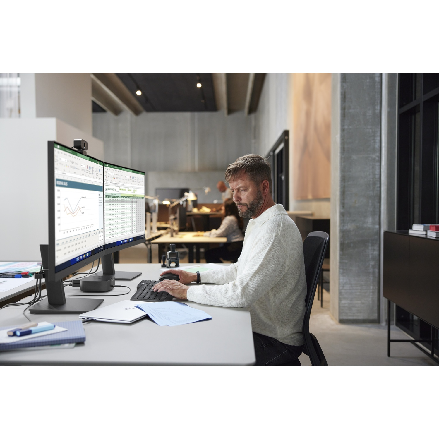 Man at desk with two monitors typing on a keyboard.