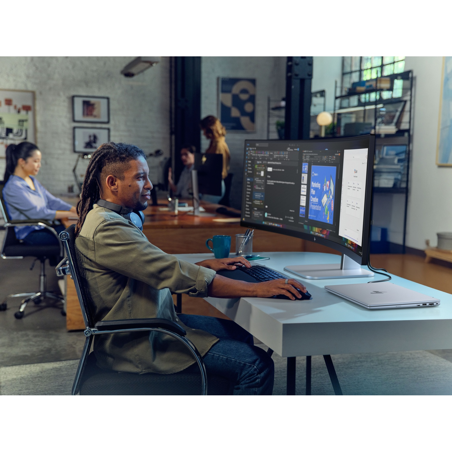 Man met dreadlocks werkt op computer in modern kantoor. Andere collega's op achtergrond.
