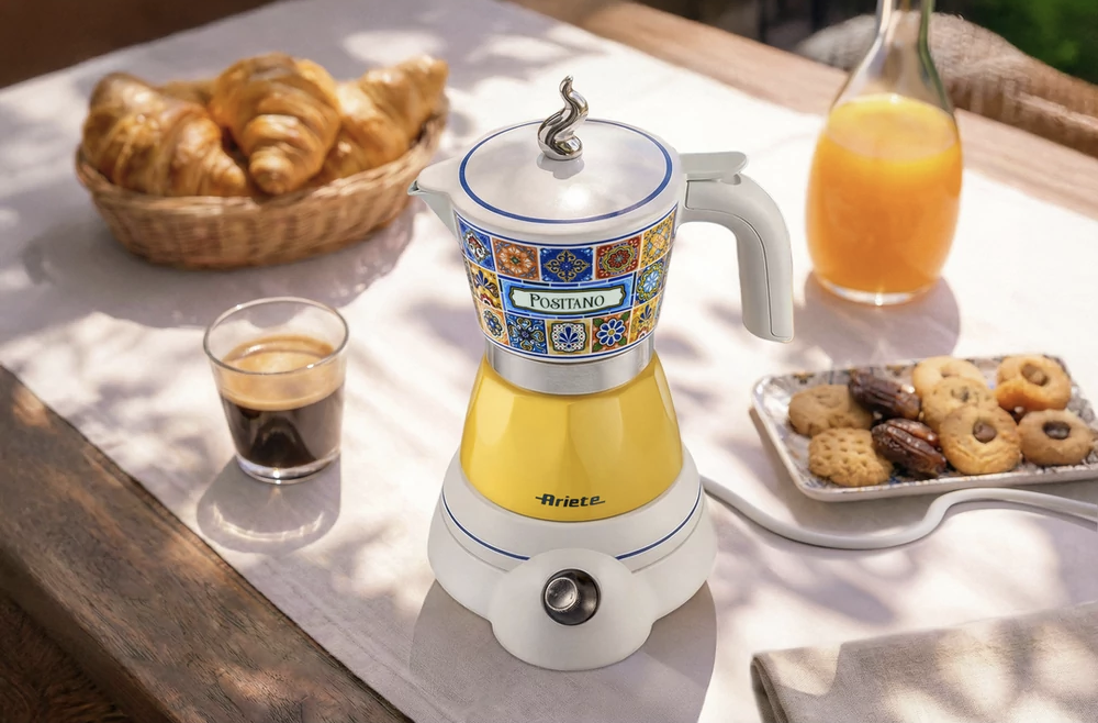 Sárga eszpresszófőző színes csempékkel, mellette kávé, croissant, keksz és narancslé.