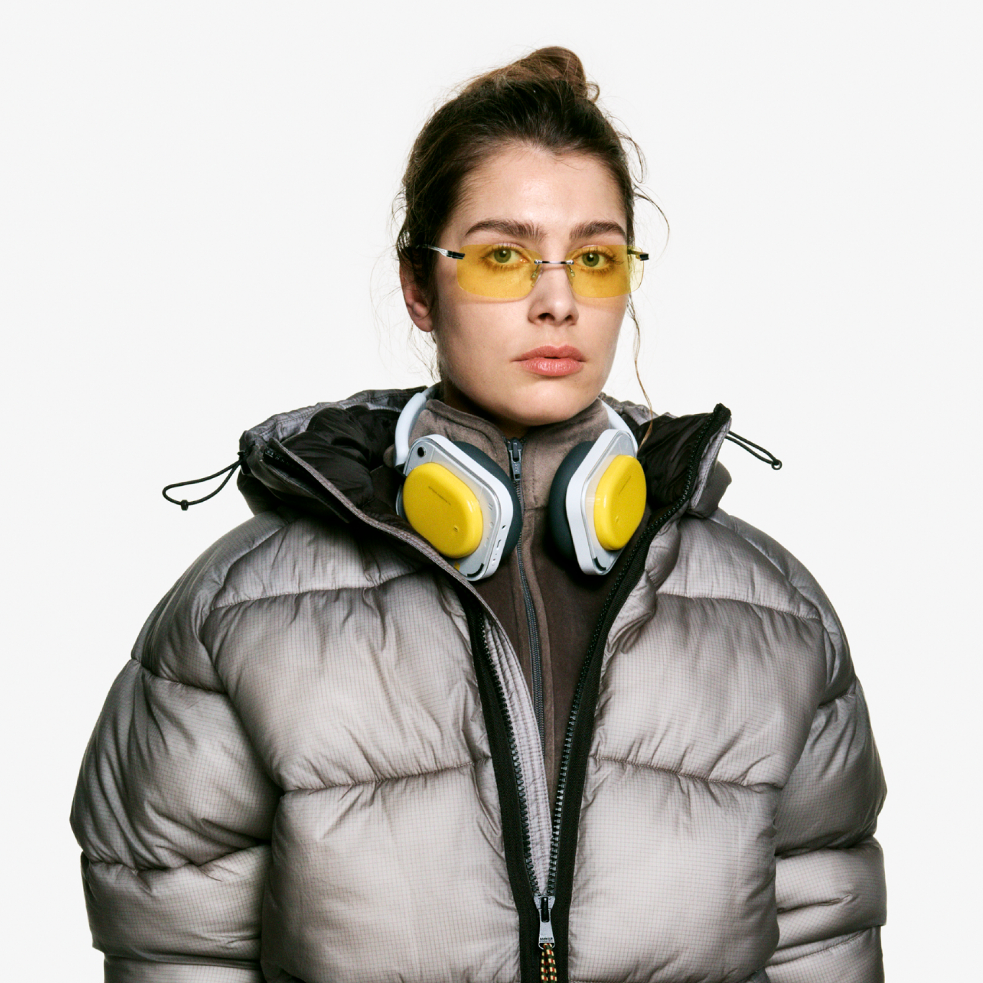 Frau mit Kopfhörern und Sonnenbrille trägt eine graue Daunenjacke.