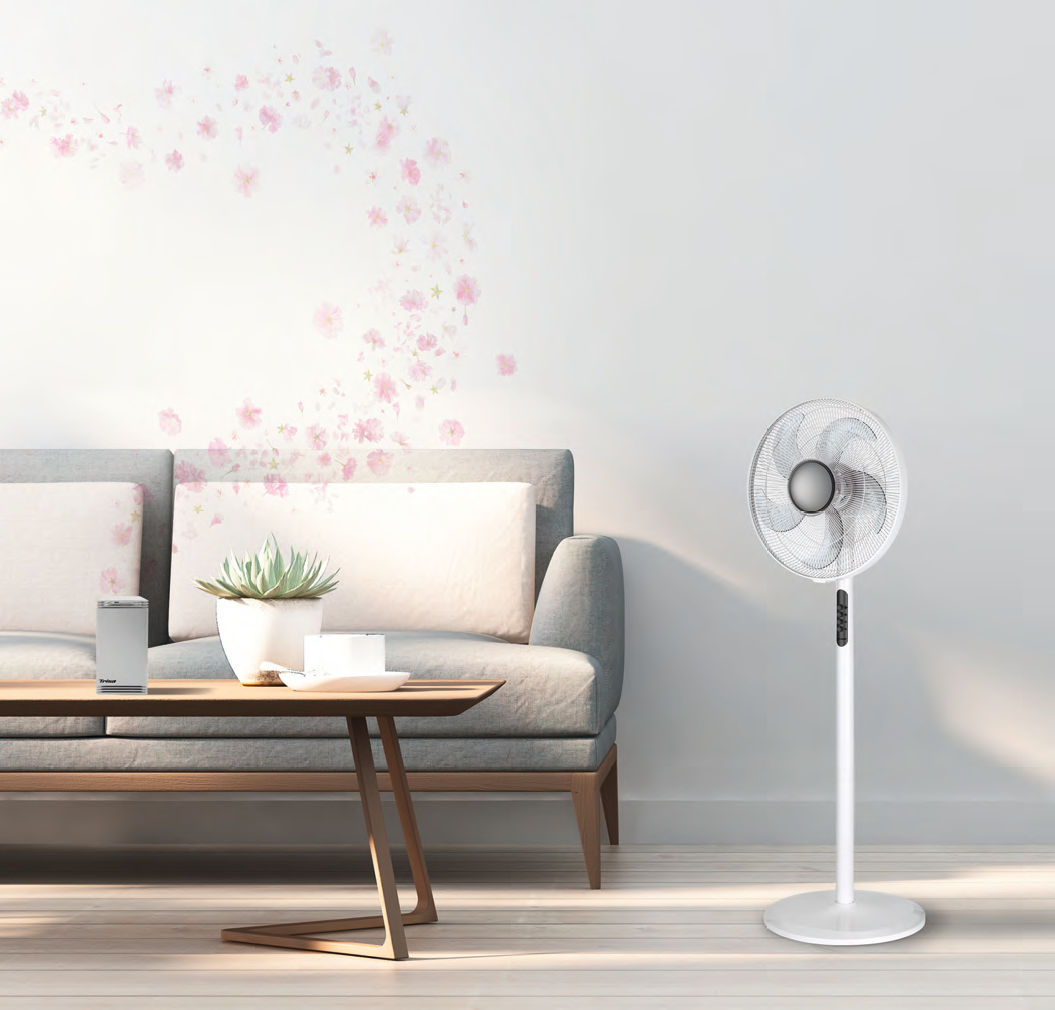 Un ventilatore da terra bianco è accanto a un divano grigio con cuscini e un tavolino.