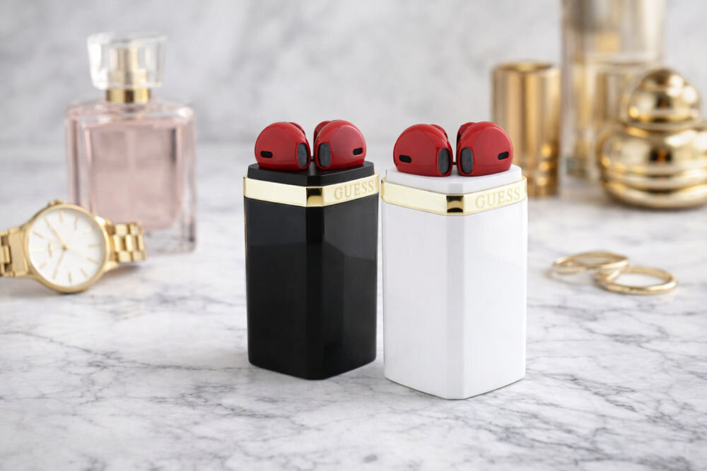 Czerwone słuchawki na czarnych i białych etui GUESS obok butelki perfum i zegarka.