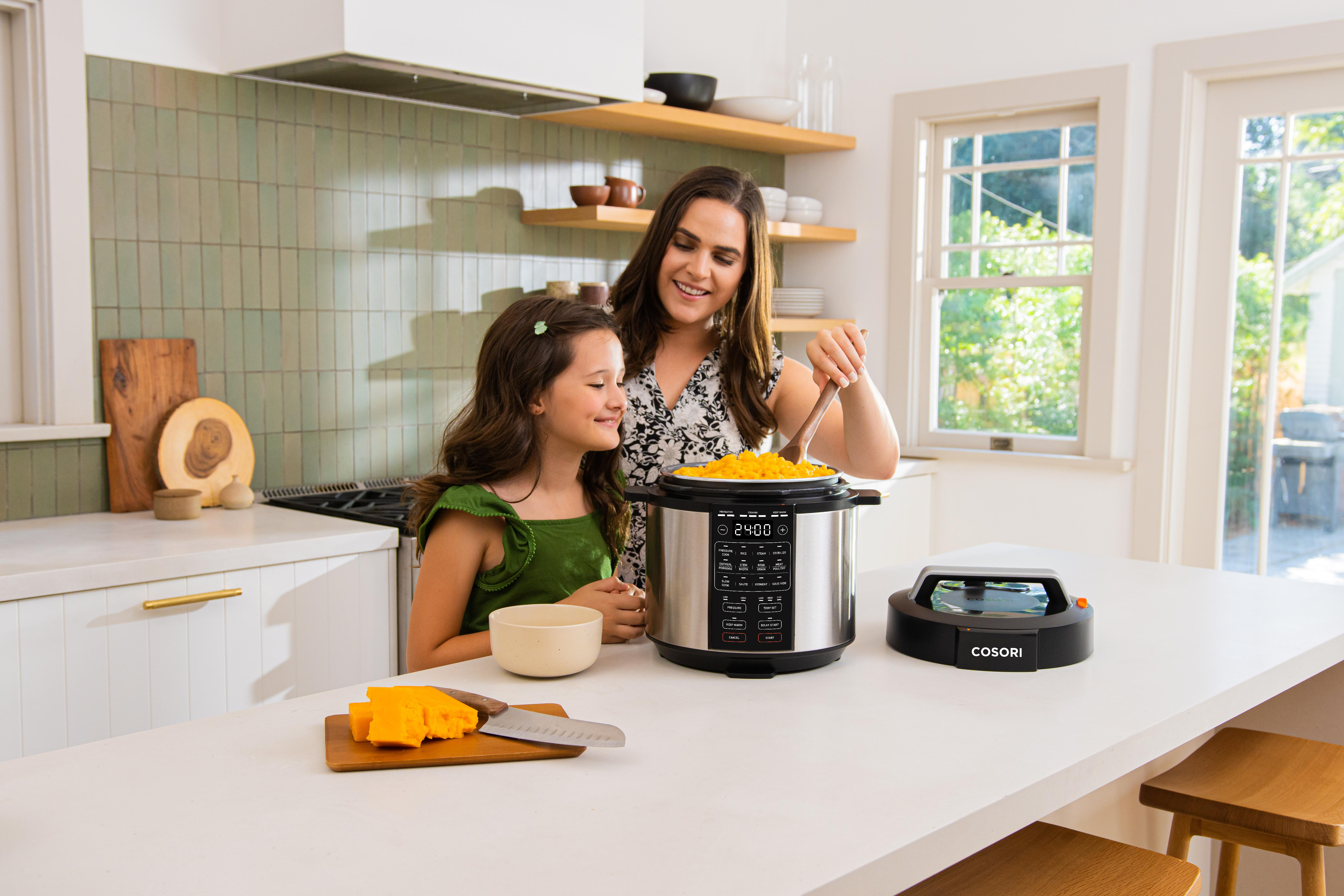 Mutter und Tochter kochen in einer Küche mit einem Schnellkochtopf und Käse.