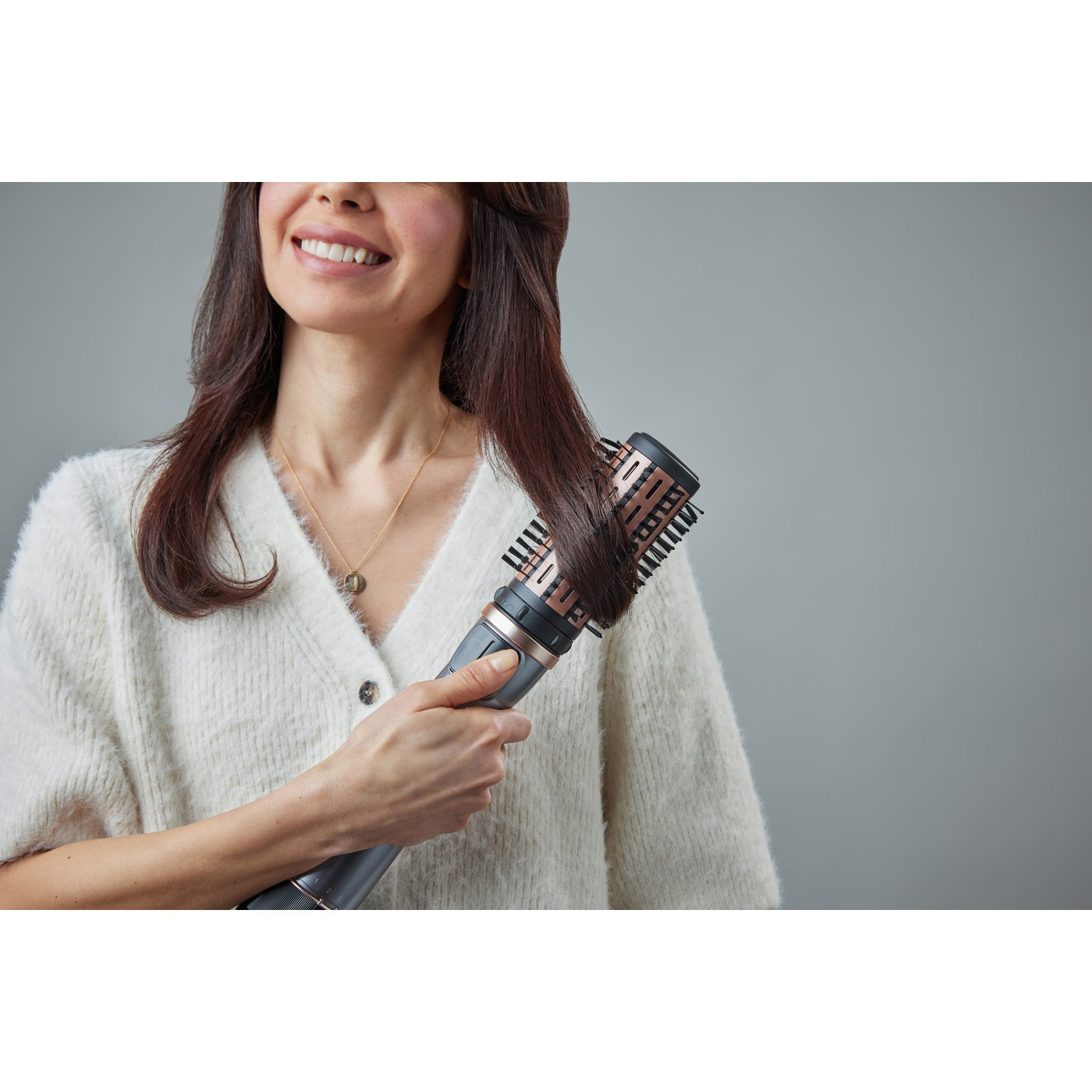 Donna con capelli castani si acconcia i capelli con una spazzola rotante.