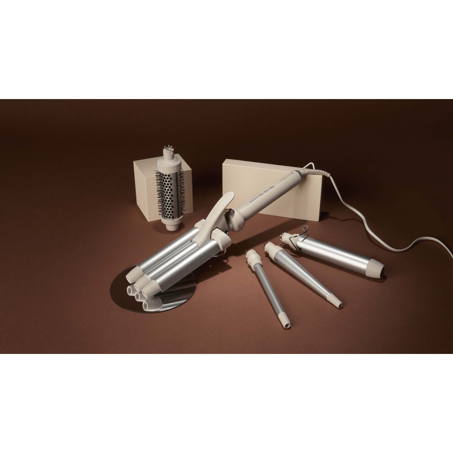Un set per lo styling dei capelli con vari accessori e un dispositivo principale su sfondo marrone.