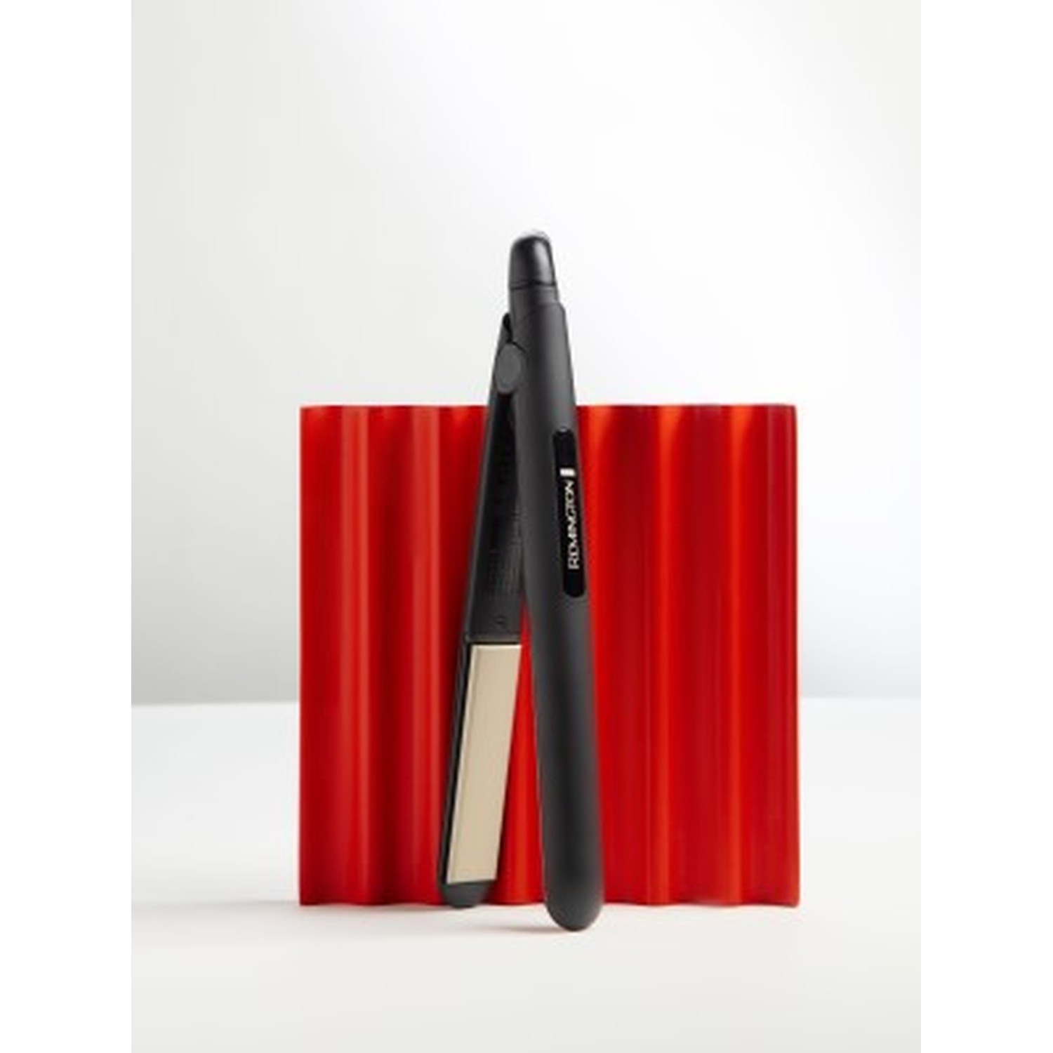 Una piastra per capelli Remington nera davanti a un oggetto rosso scanalato.