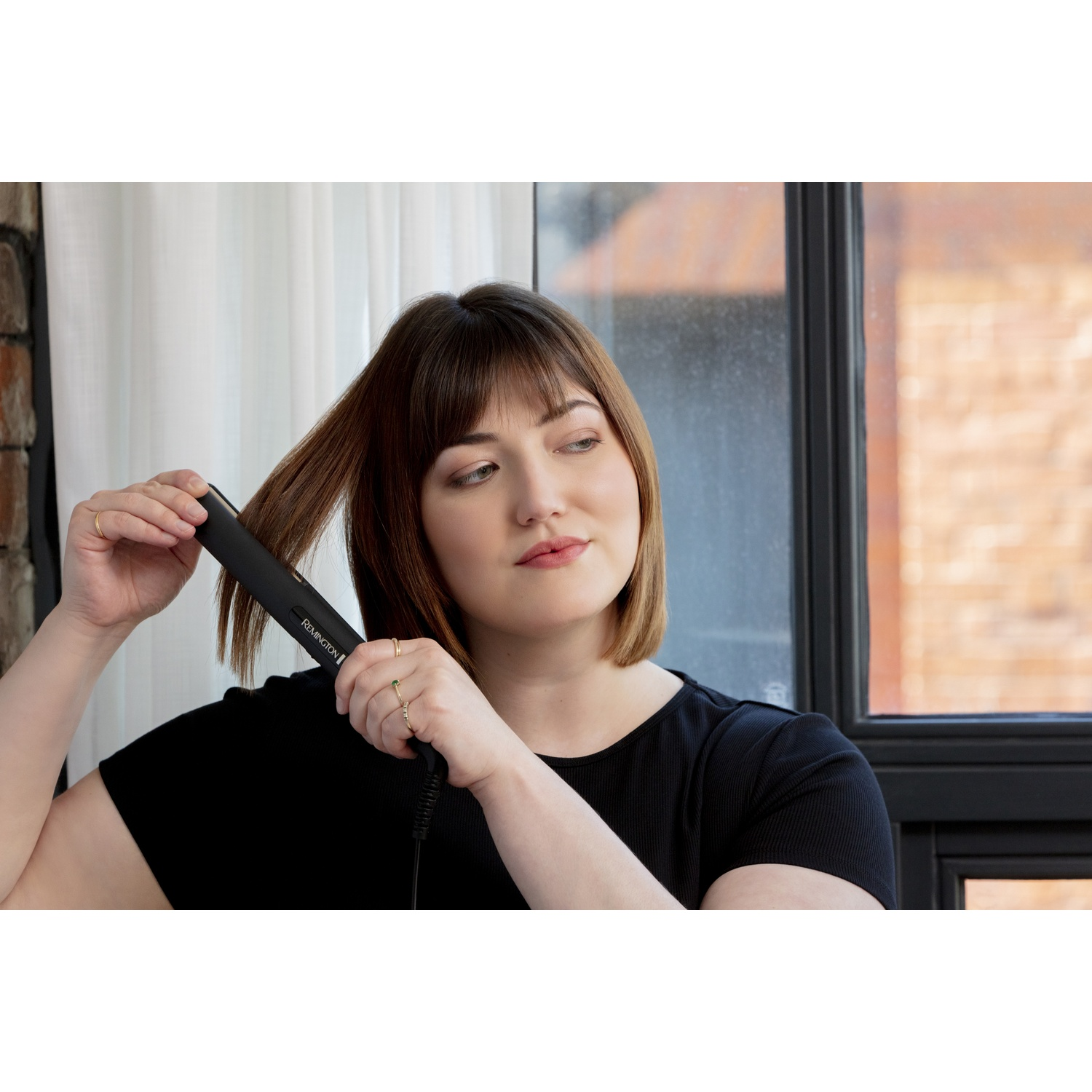 Una donna si liscia i capelli castani con una piastra nera.