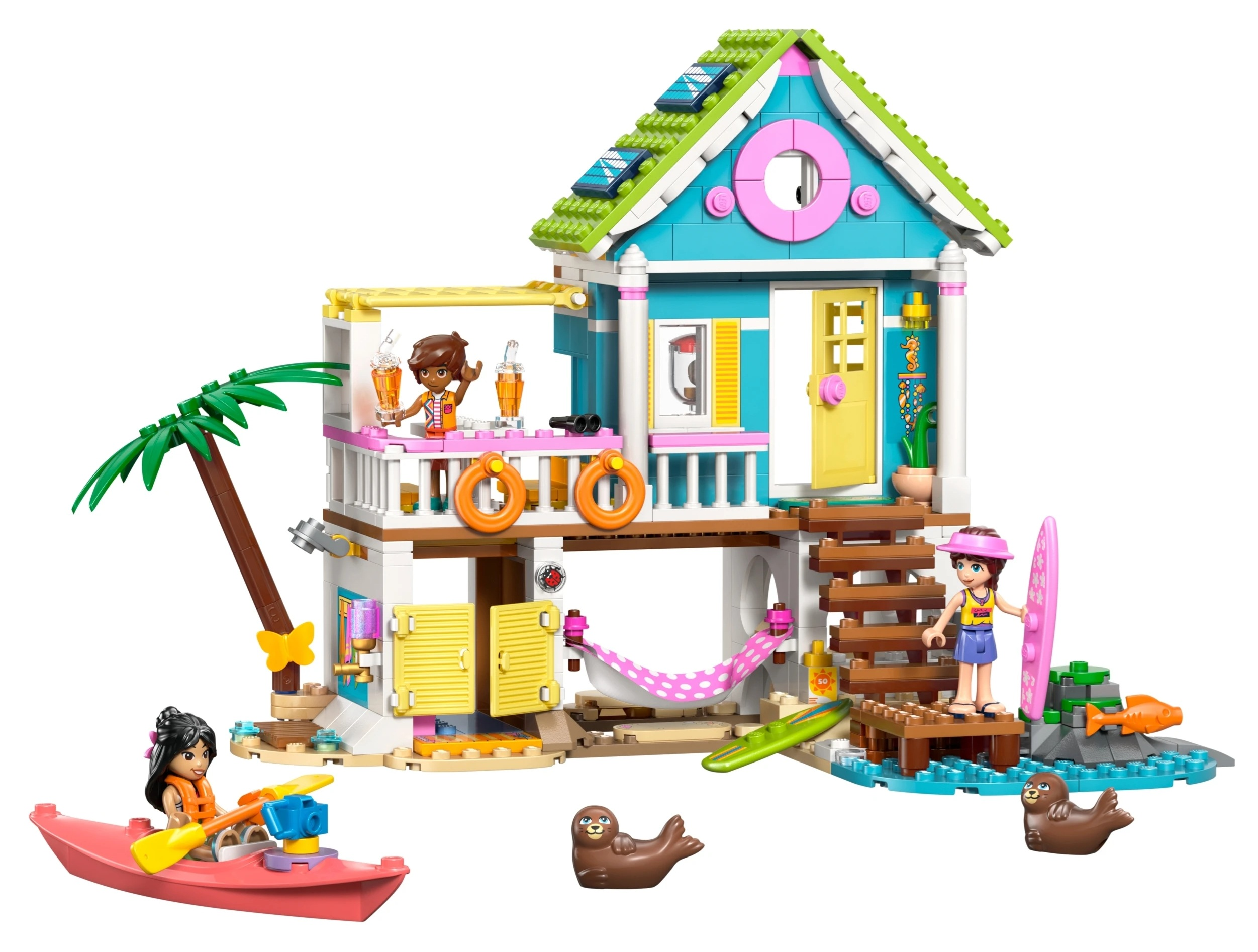 Kolorowy dom plażowy Lego z palmą, postaciami, kajakiem, deską surfingową i fokami.