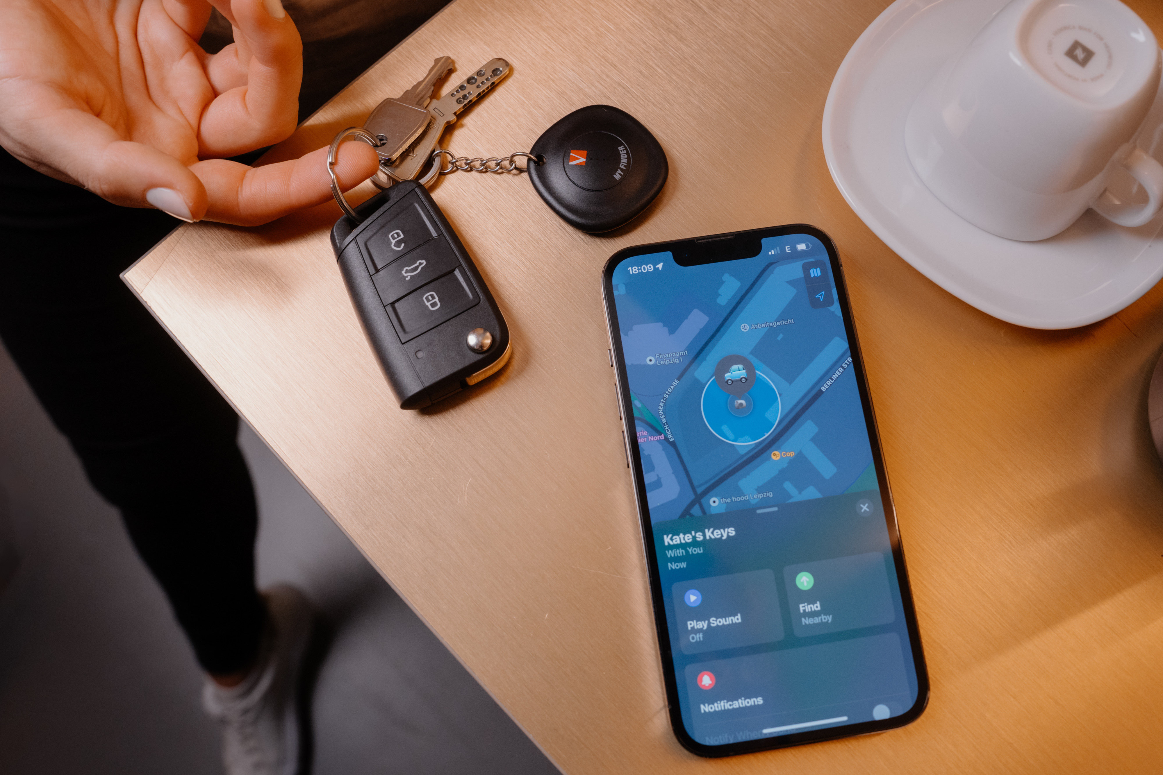 Schlüsselbund mit Autoschlüssel, Tracker und Handy mit Karten-App auf Holztisch.