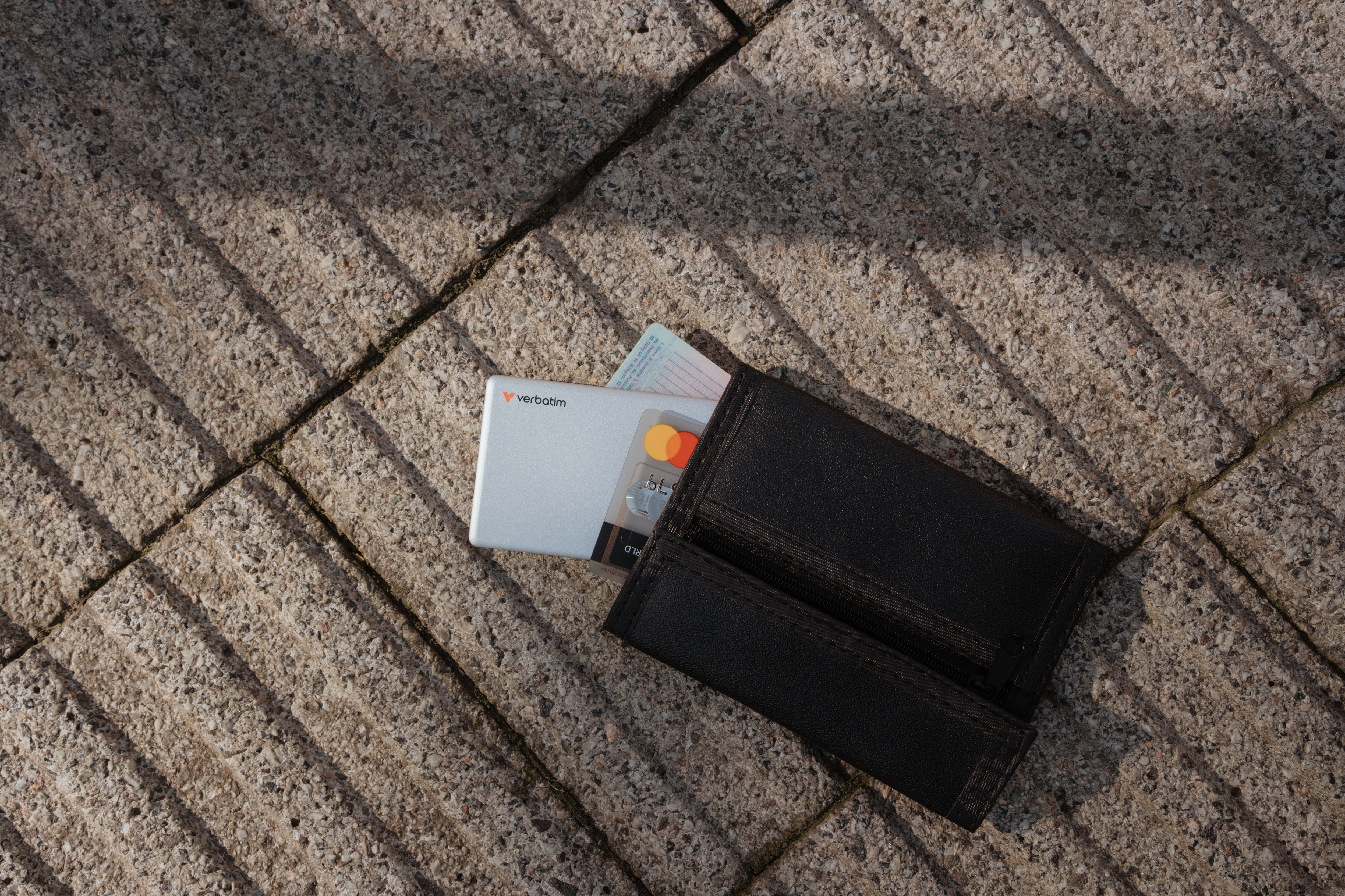 Ein schwarzes Portemonnaie mit einer silbernen Speicherkarte und Kreditkarten auf Steinfliesen.