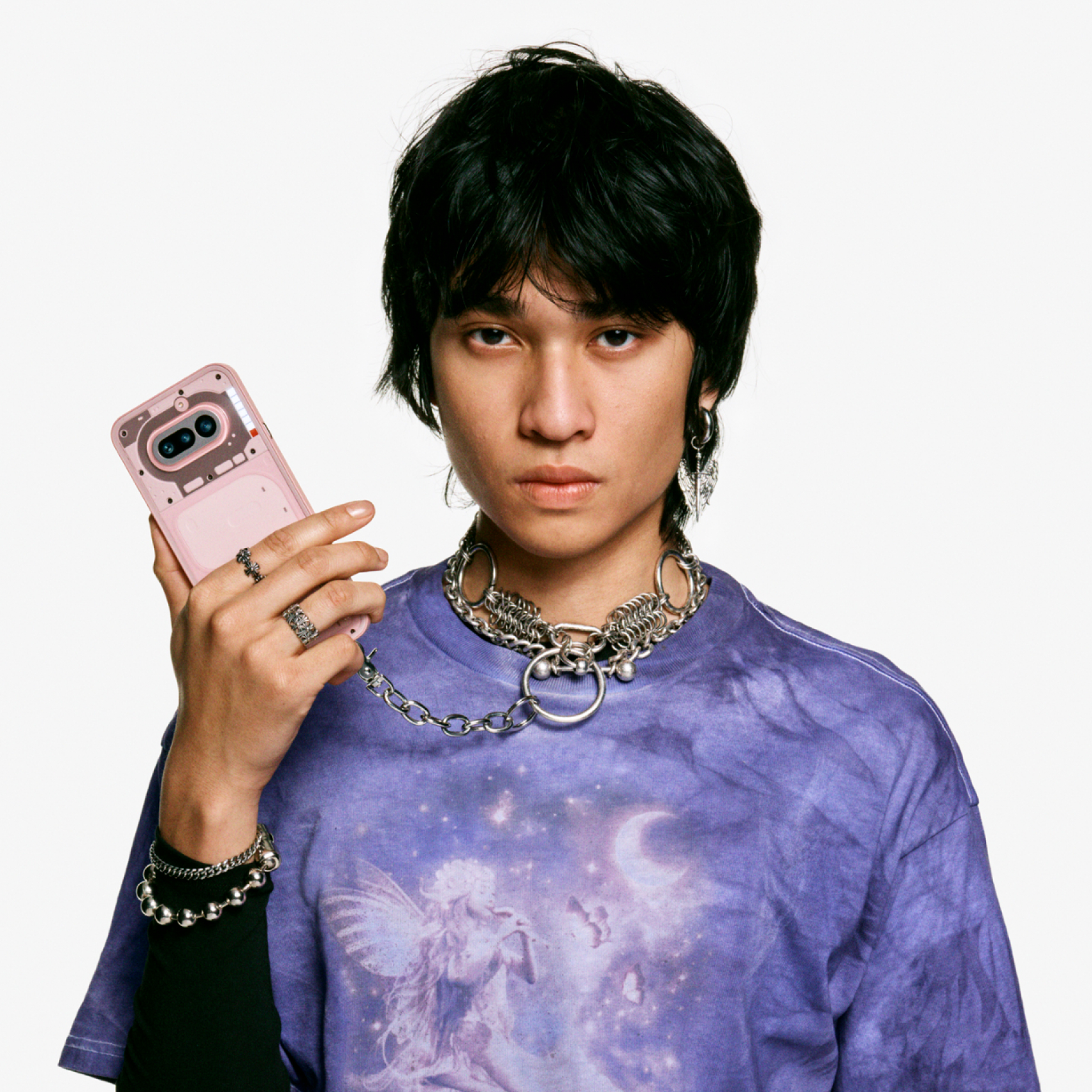 Jeune personne aux cheveux noirs tient un smartphone rose. Porte un t-shirt violet.