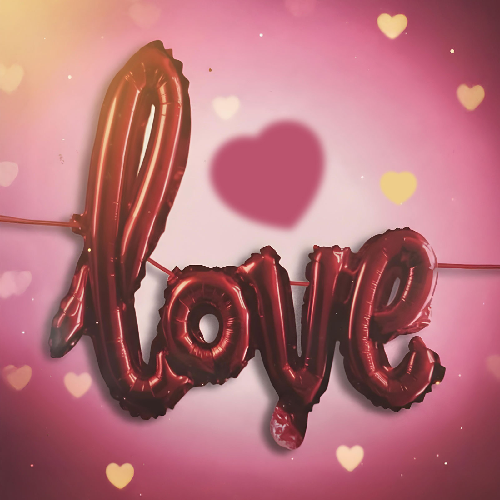 Piros fólia lufikból kirakott „Love” felirat rózsaszín háttérrel, szívekkel.