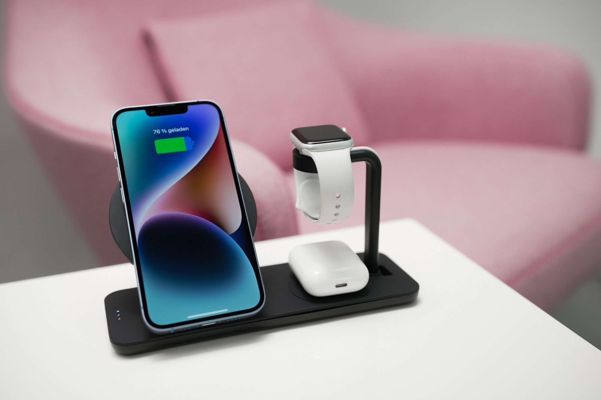 Czarna stacja ładująca z iPhonem, Apple Watch i AirPods na białym stole.