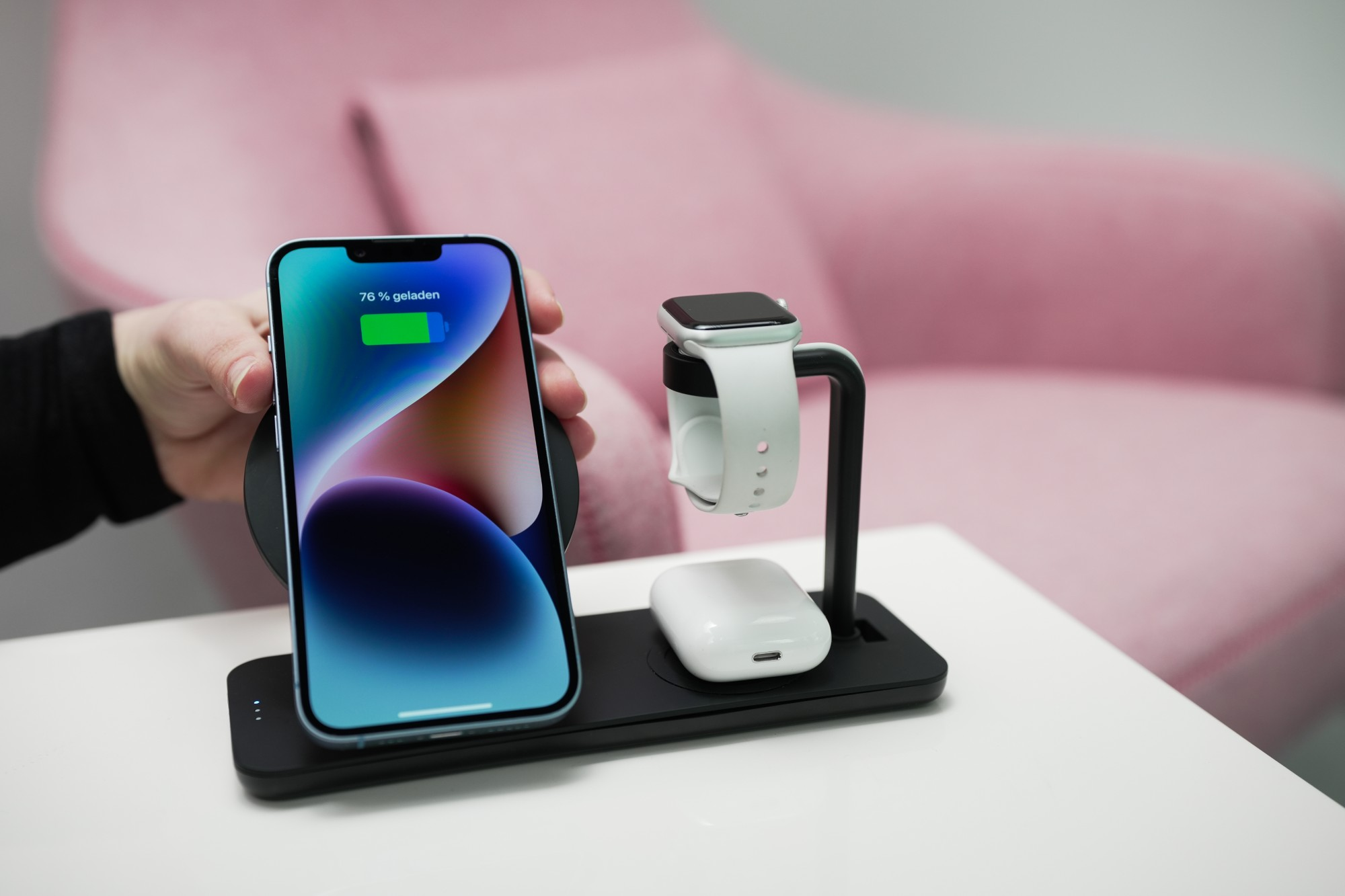 iPhone ładuje się na czarnej stacji dokującej z Apple Watch i AirPods obok.