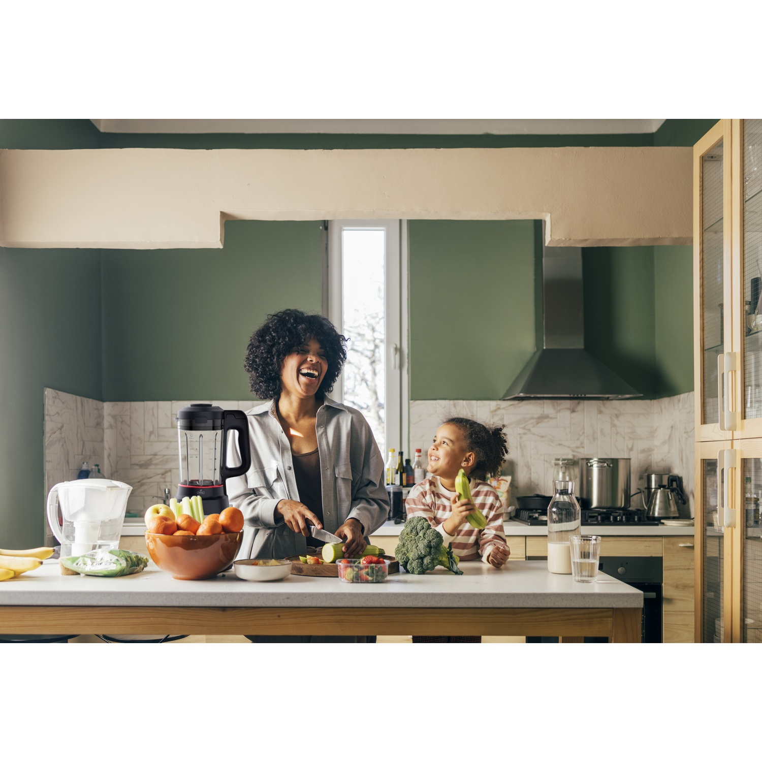 Een vrouw en kind bereiden eten in een keuken. Fruit en groenten liggen op het aanrecht.