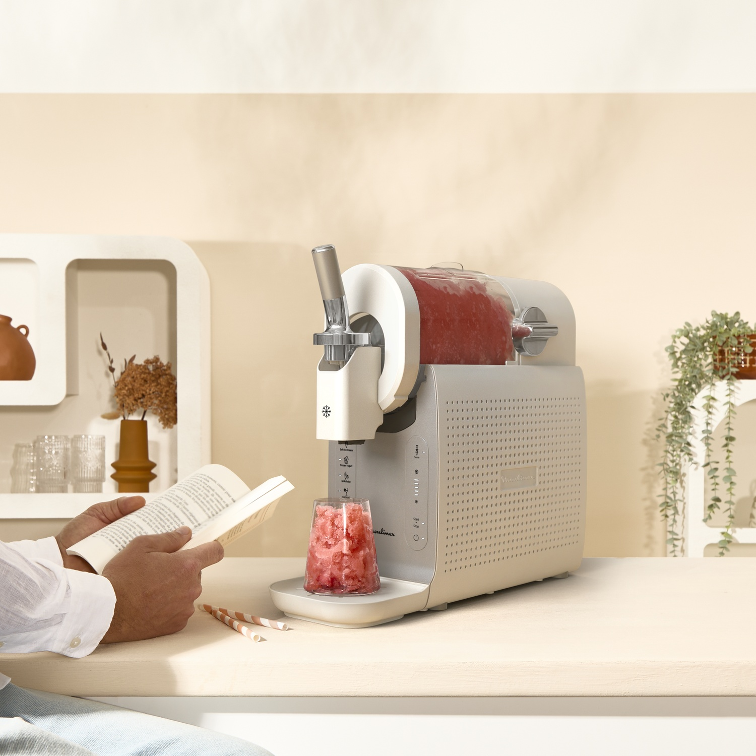 A man reads a book next to a slush machine with frozen fruit.