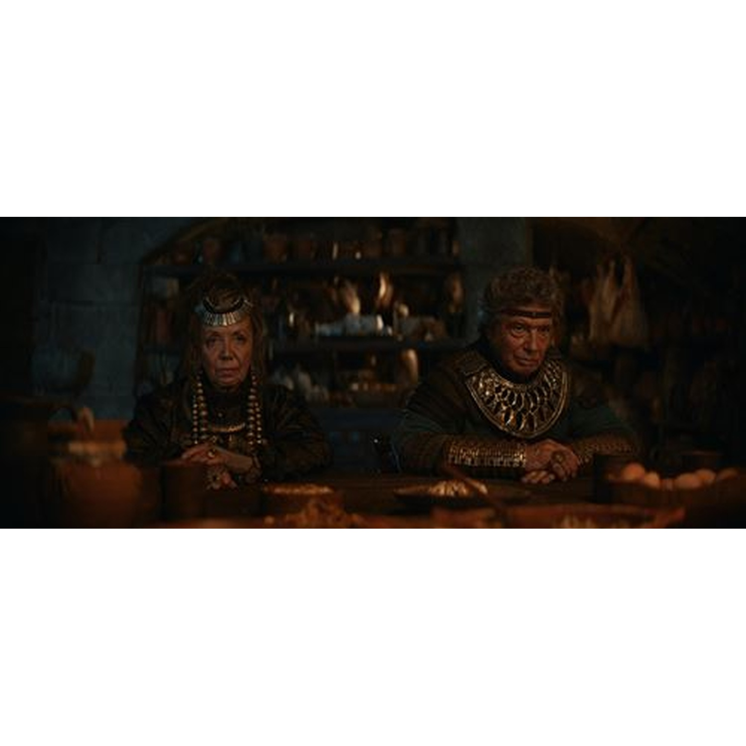 Un homme et une femme sont assis à une table en bois avec de la nourriture. Ils portent des vêtements historiques.