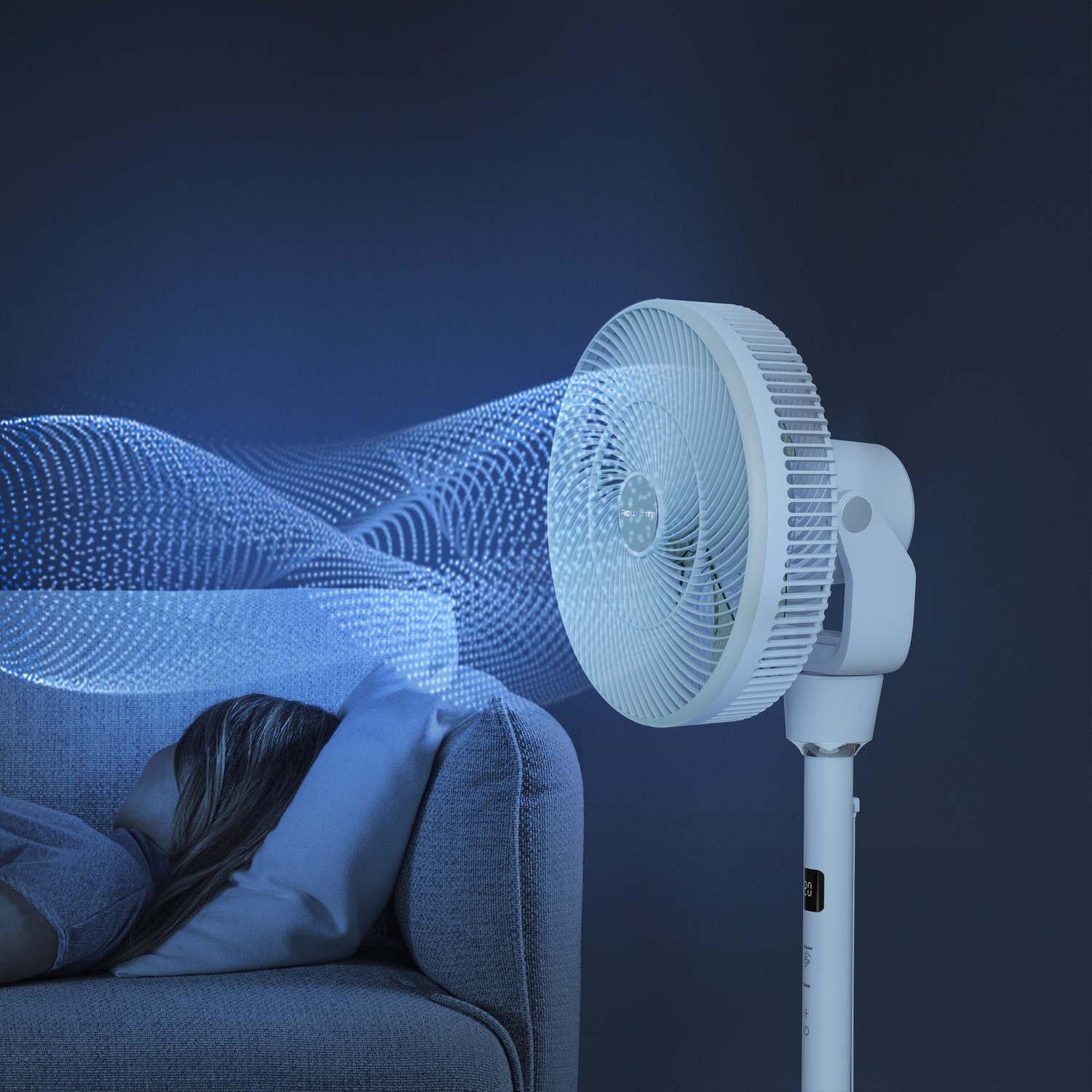 Een witte ventilator blaast lucht naar een slapend persoon op een bank.