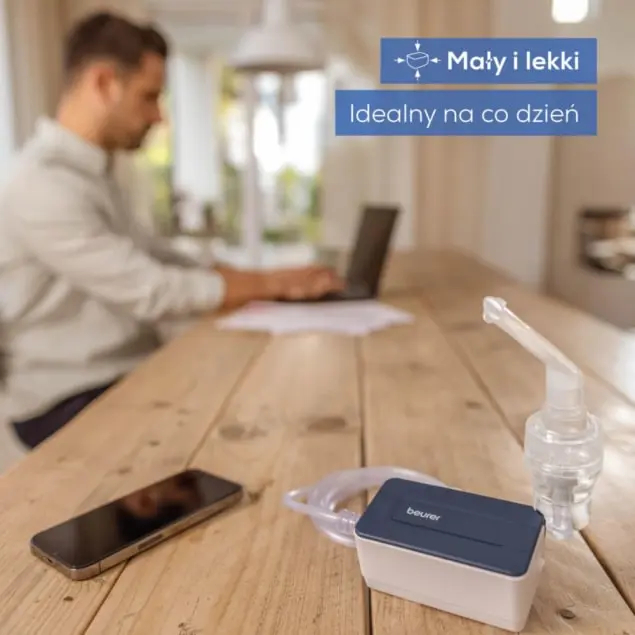 Mężczyzna pracuje przy laptopie, obok niego nebulizator, telefon i rurka.