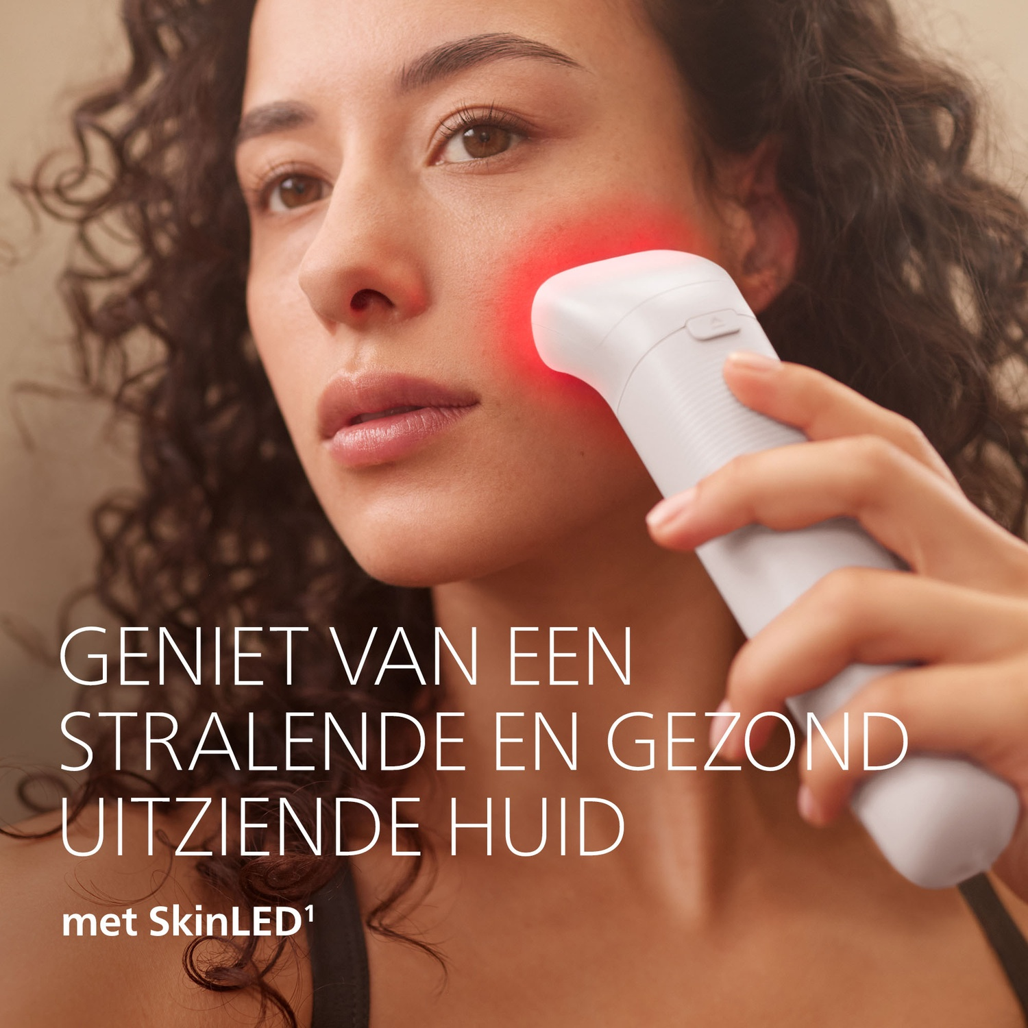 A woman uses a red light skin care device on her cheek.